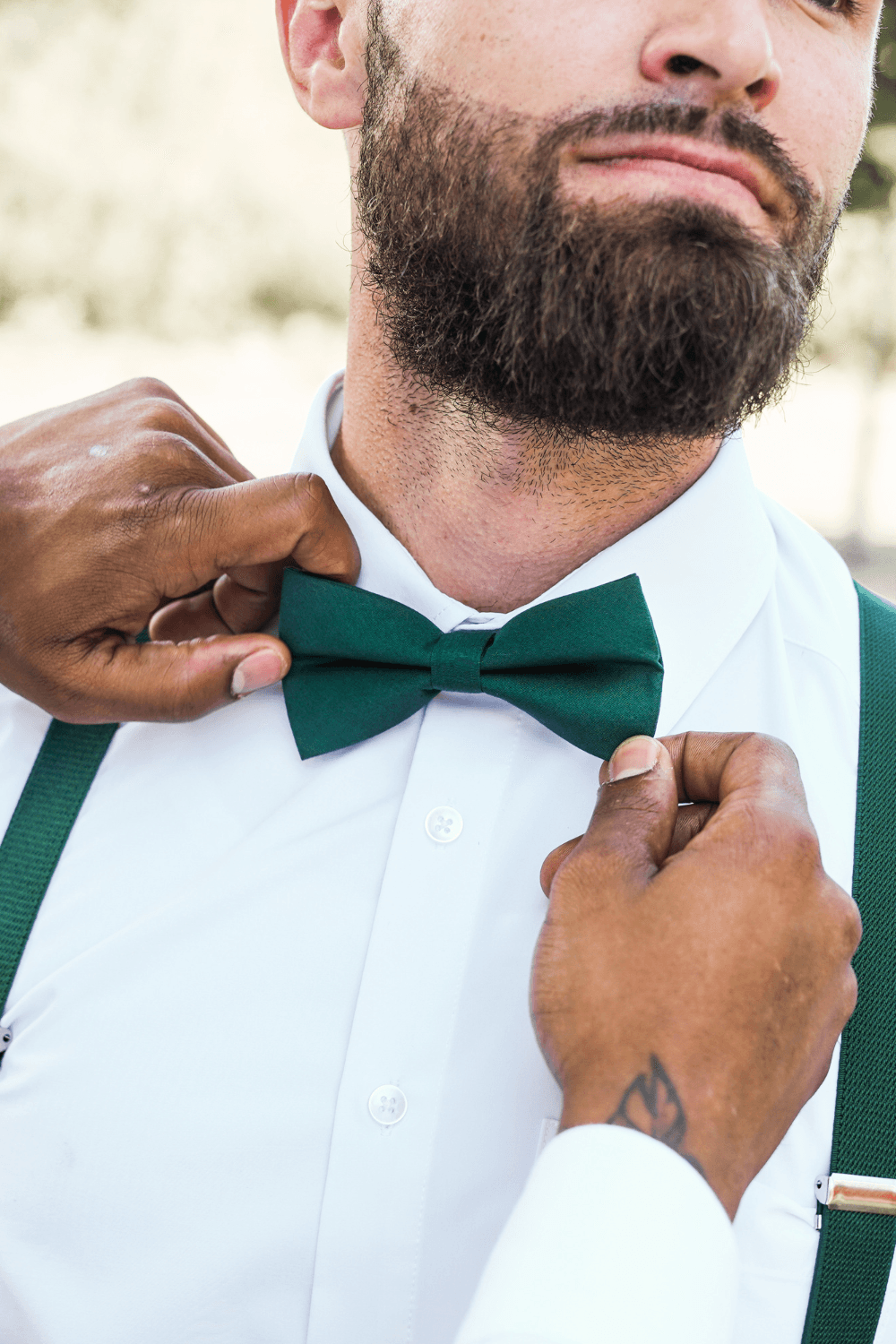 Groomsman wearing dark green suspenders and putting on a juniper green bow tie for a wedding.