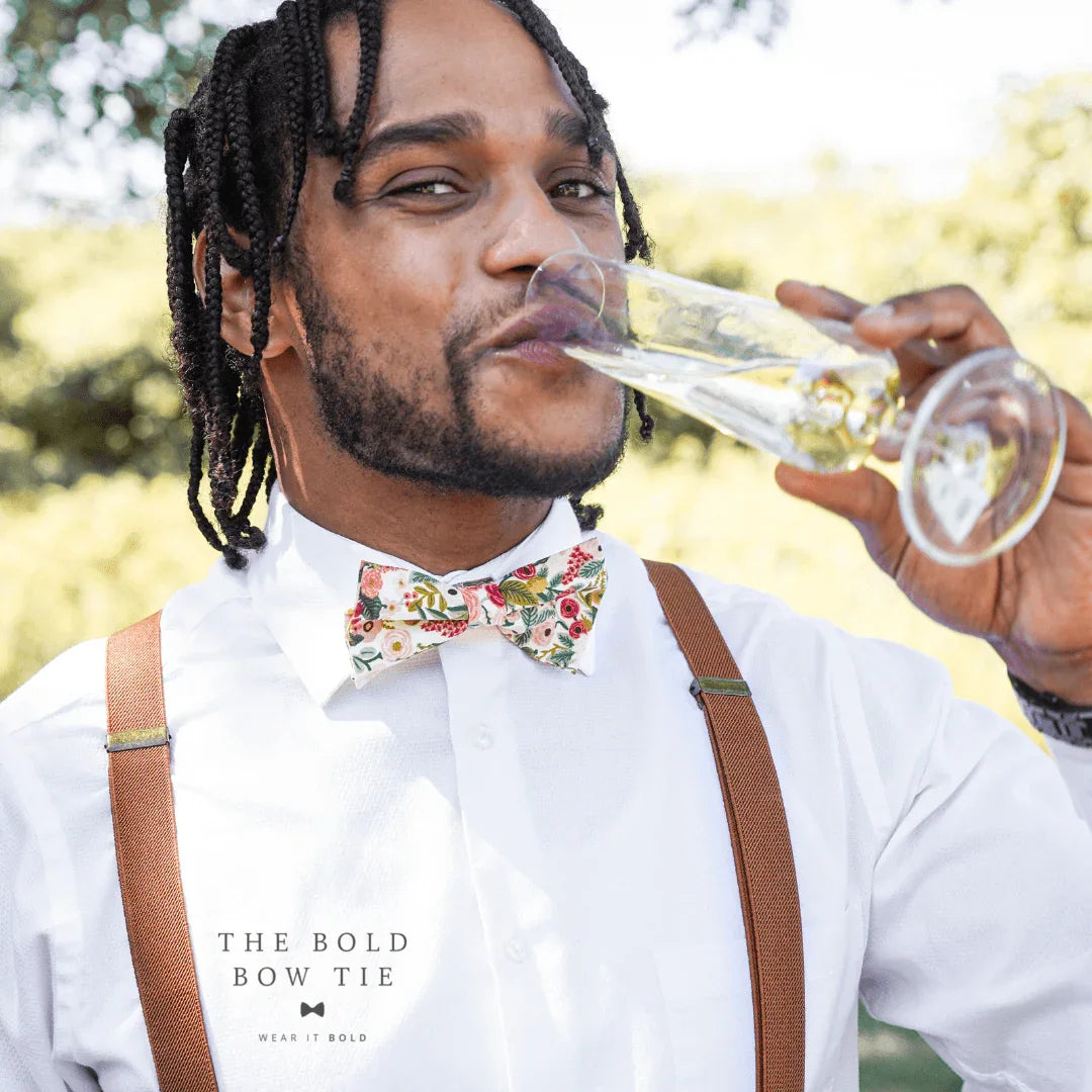 Portrait of a man outdoors wearing a floral bow tie and olive suspenders over a white shirt.
