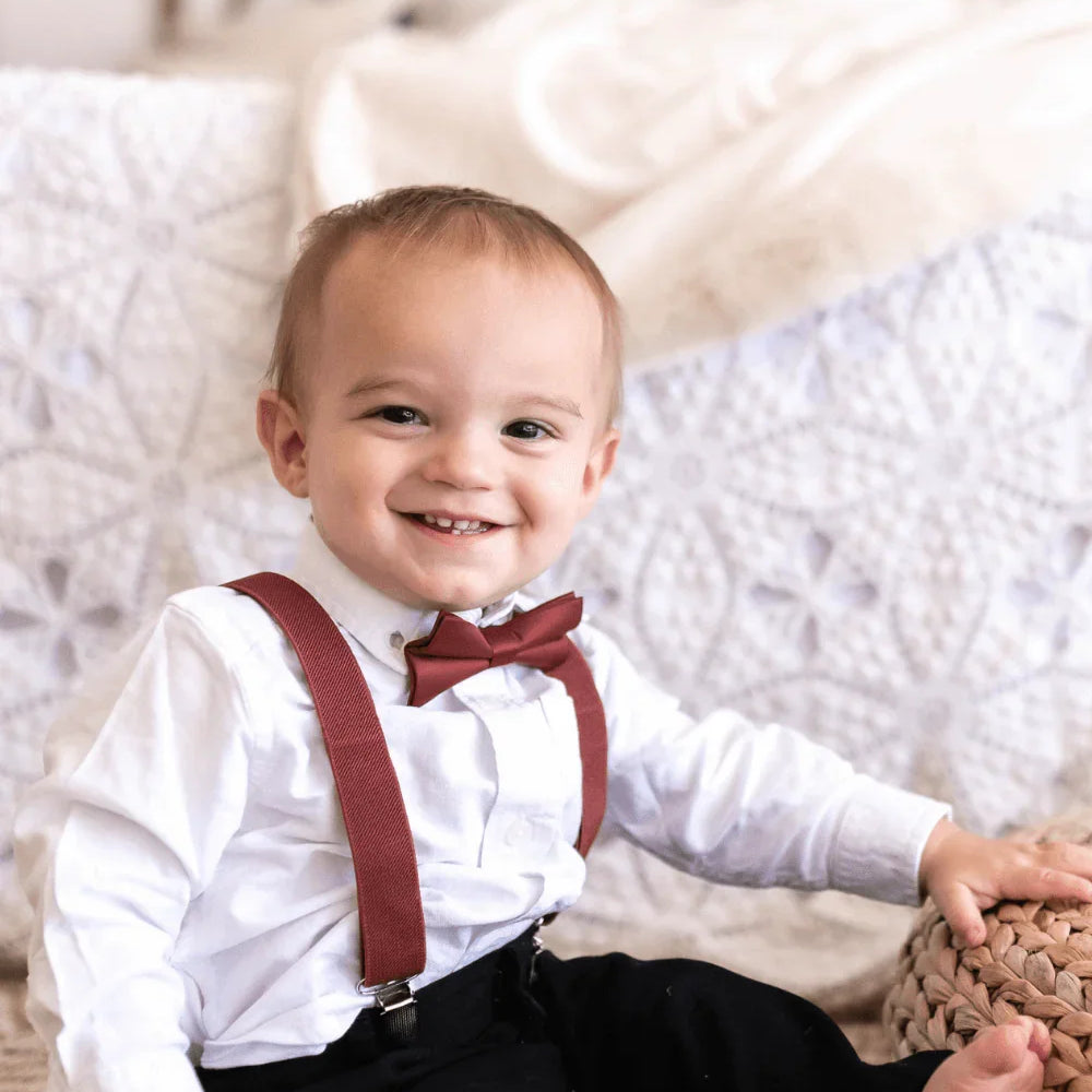 Ring bearer in cinnamon bow tie and suspenders getting ready to walk down the aisle at a wedding.