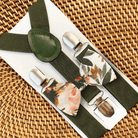A set of olive green elastic suspenders with a floral bow tie on a woven background.