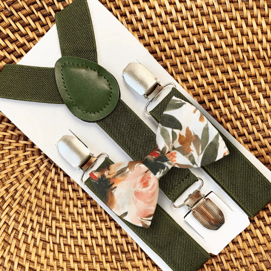 A set of olive green elastic suspenders with a floral bow tie on a woven background.