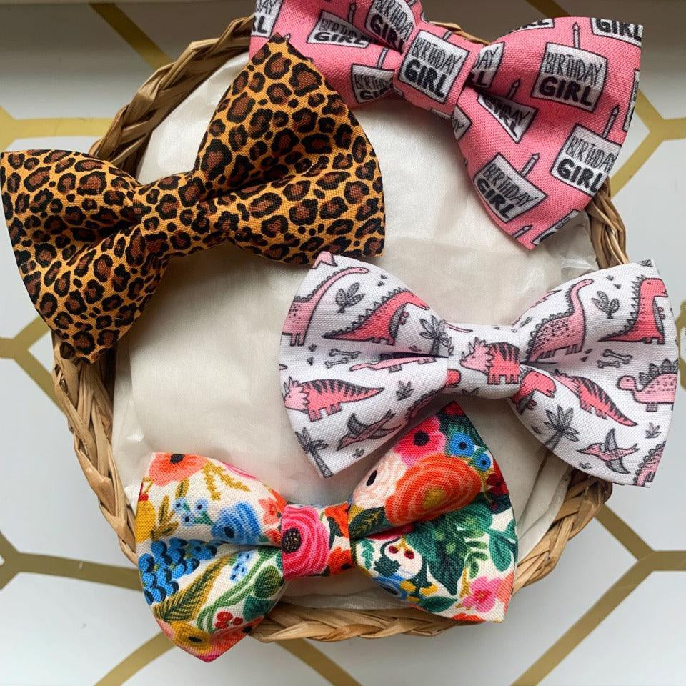 Three bows in a basket including pink Birthday Girl bow, white bow with pink dinosaur pattern, and a colorful floral bow