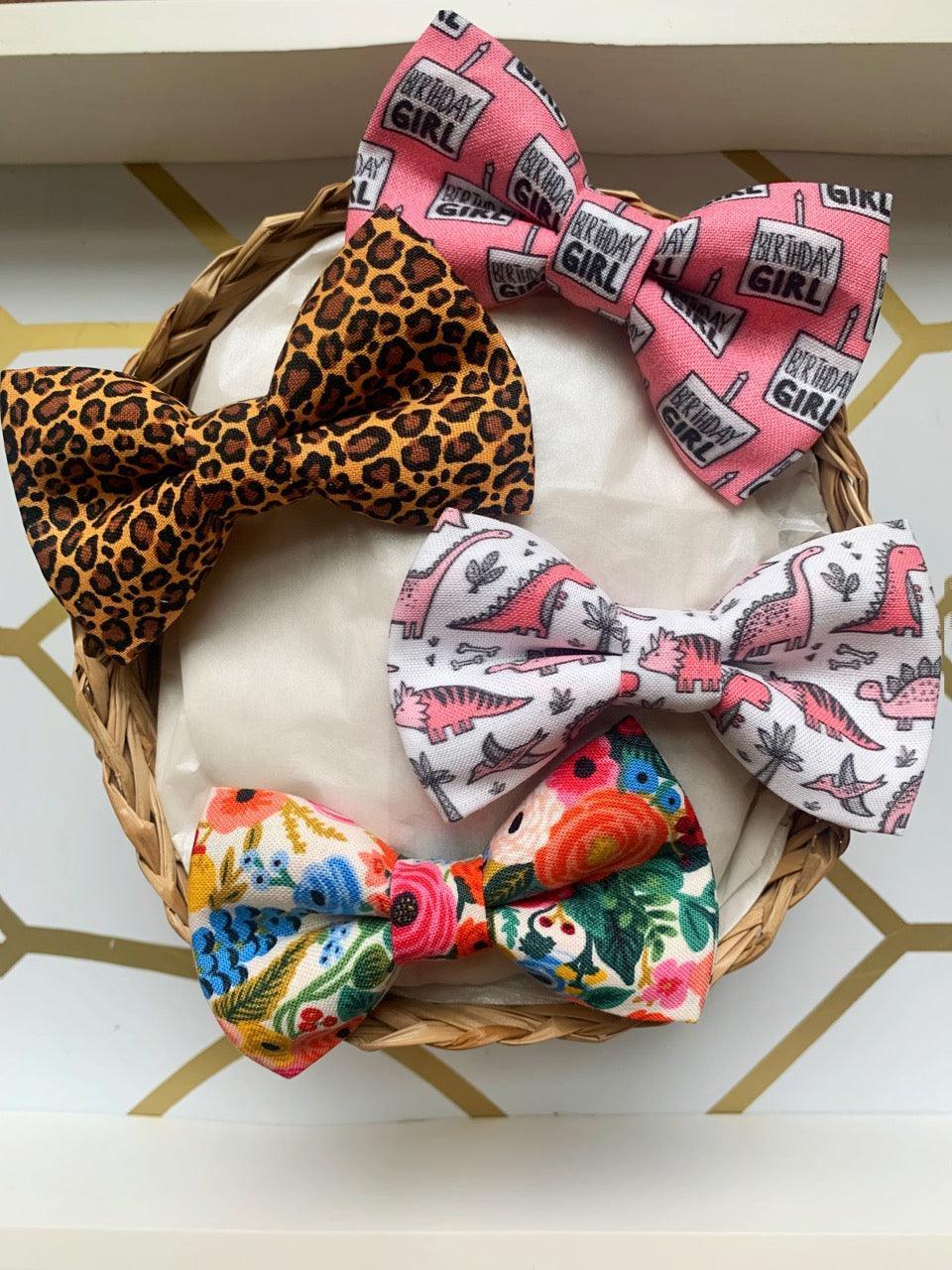 Three bows in a basket including pink Birthday Girl bow, white bow with pink dinosaur pattern, and a colorful floral bow