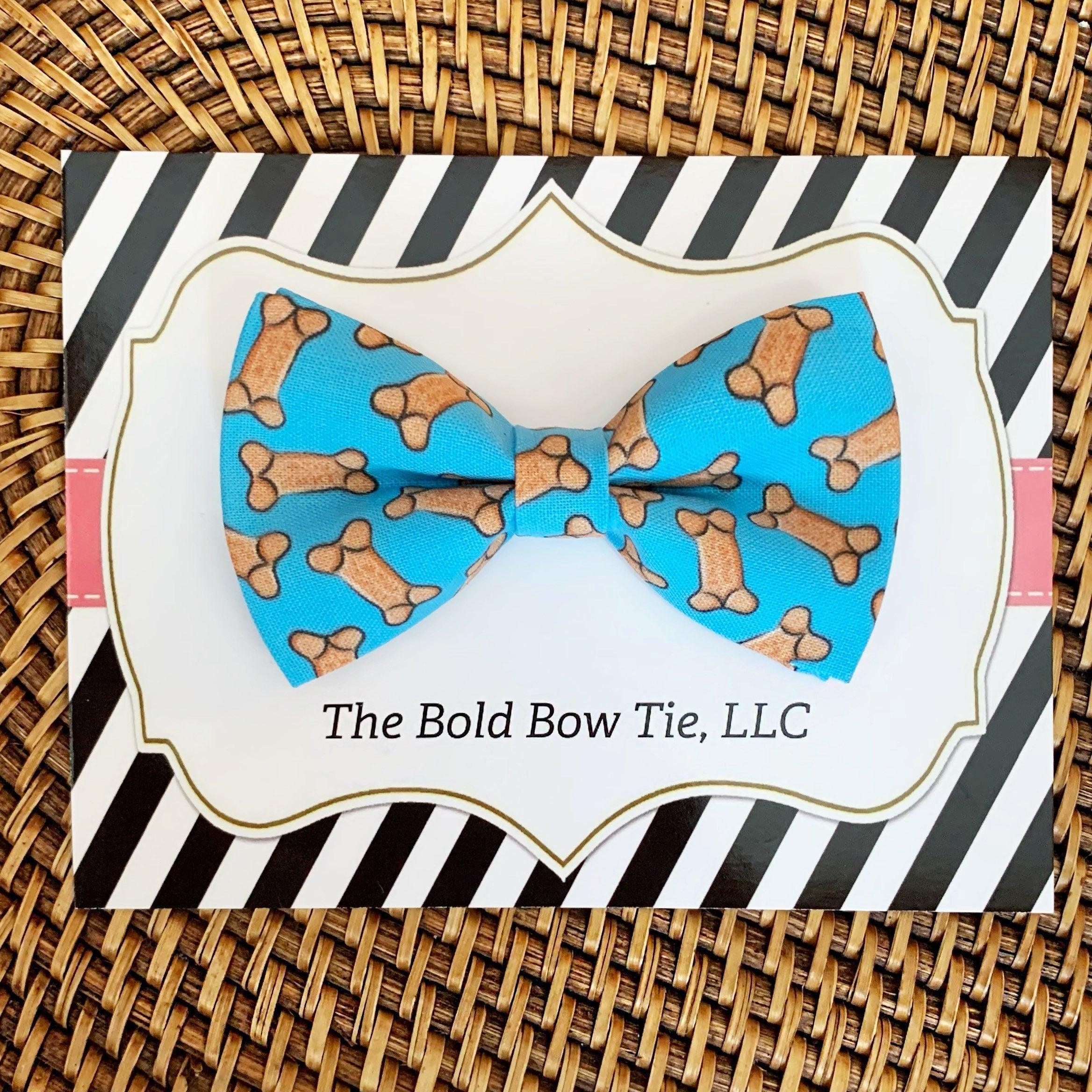Dog bow tie in blue with bone pattern on a white card inside striped black and white packaging.