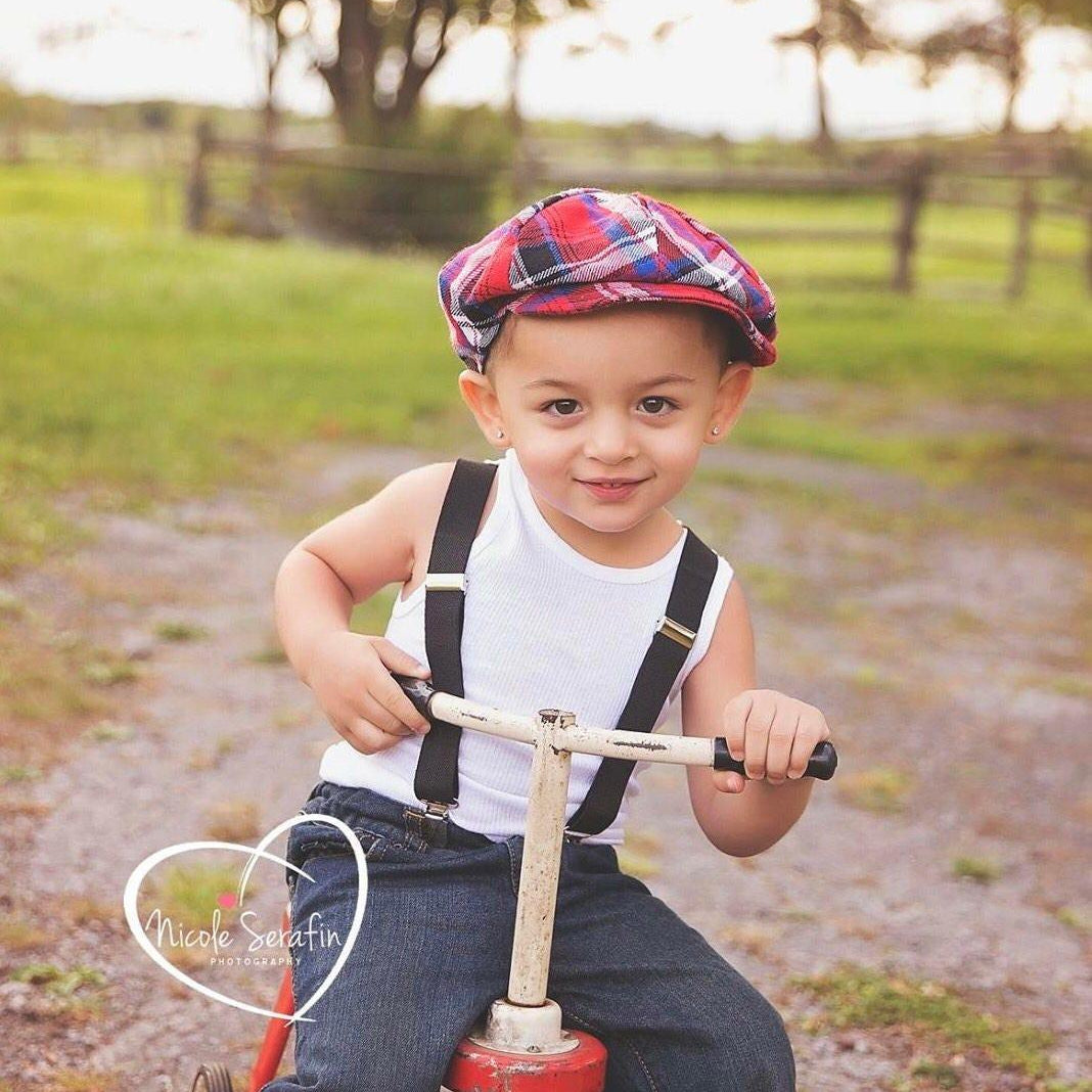 Toddler in dark gray suspenders riding a red trike.