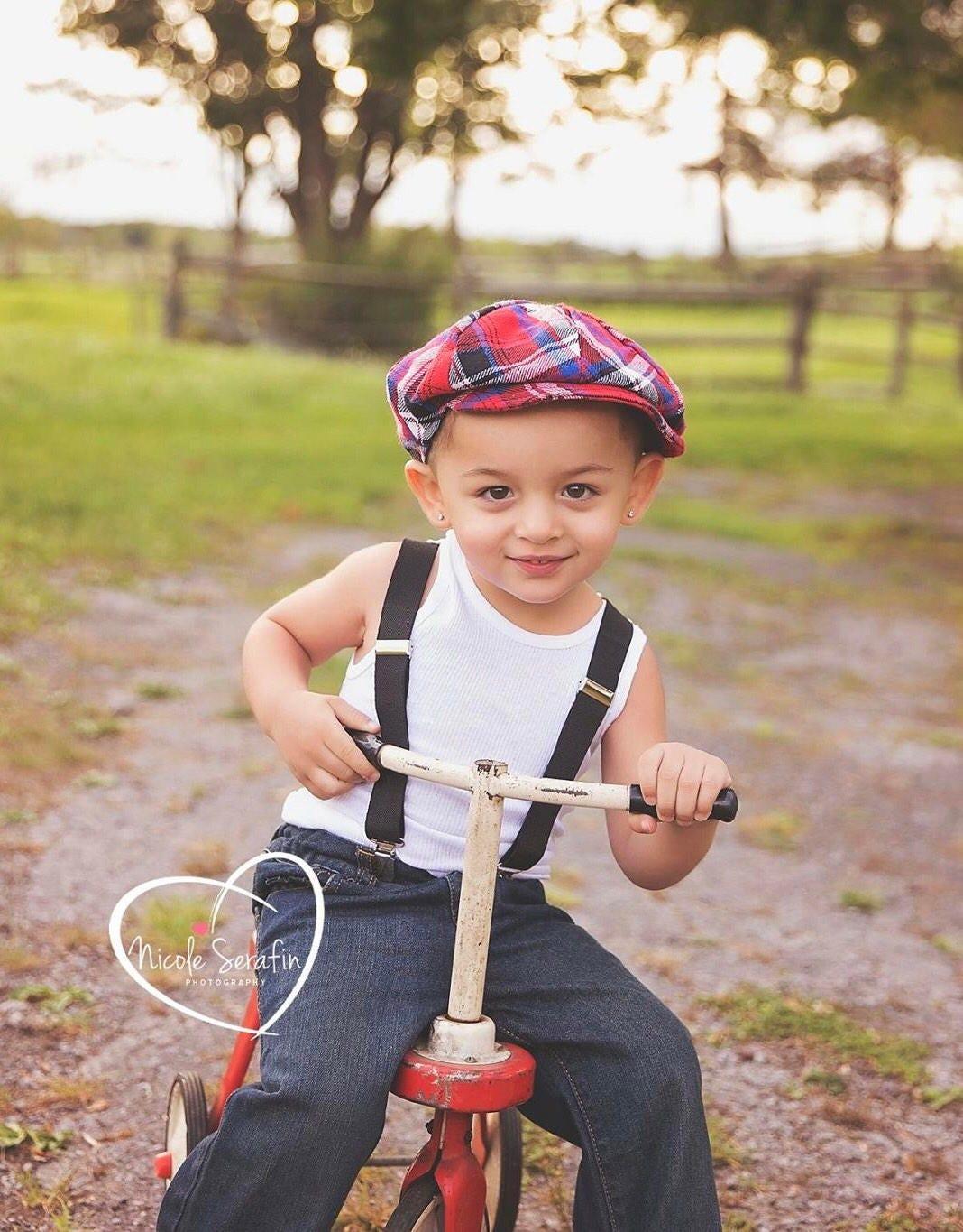 Toddler in dark gray suspenders riding a red trike.