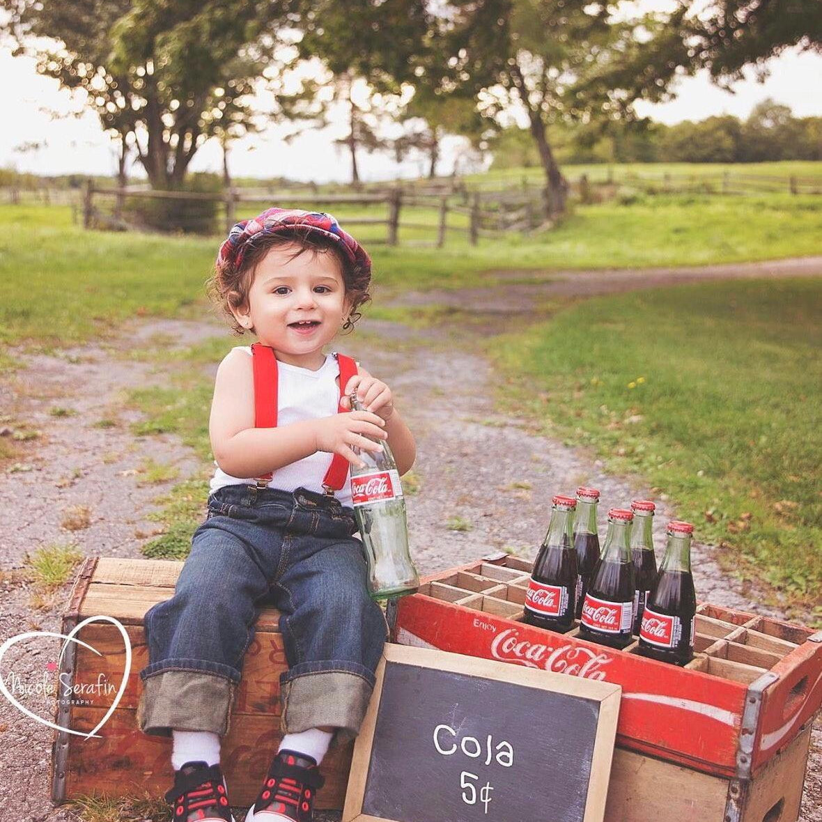 Boy holding an old bottle wearing red suspenders and newsboy cap.