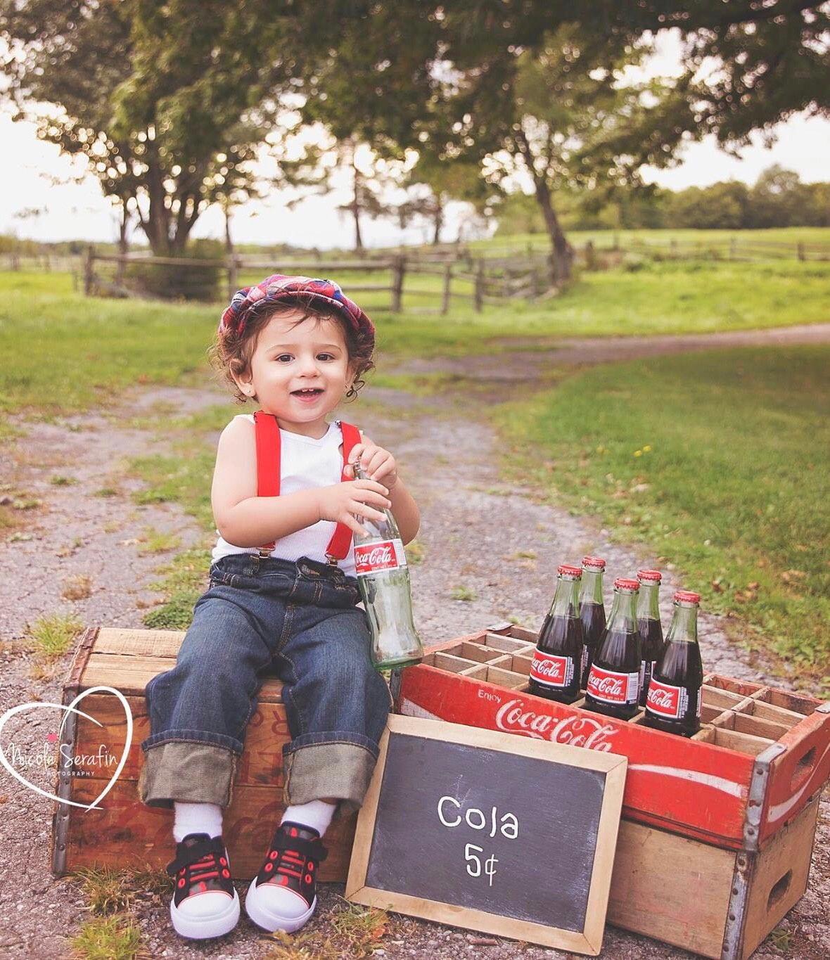 Boy holding an old bottle wearing red suspenders and newsboy cap.