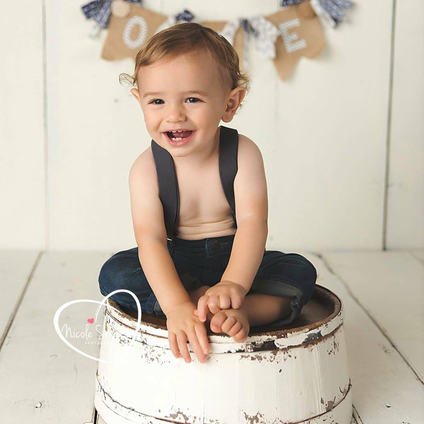 Baby wearing dark gray suspenders at a first birthday photo shoot.