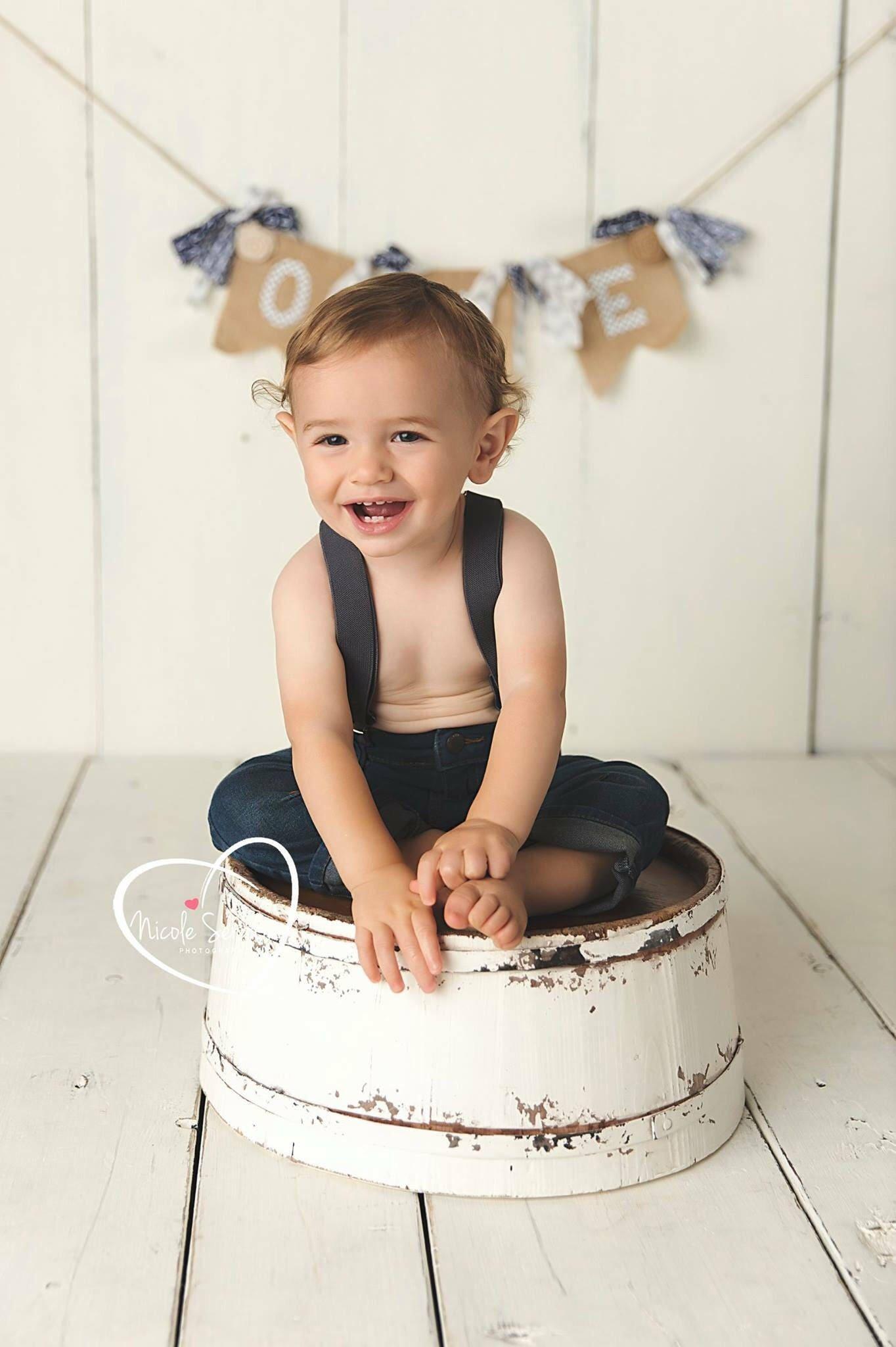 Baby wearing dark gray suspenders at a first birthday photo shoot.