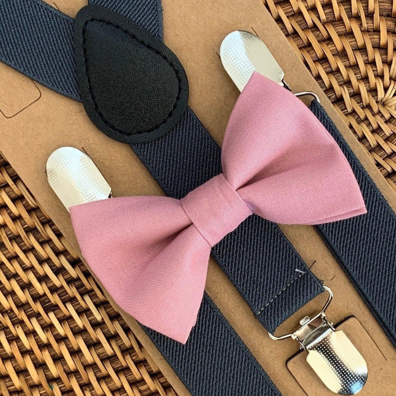 Pink bow tie with gray suspenders on a woven surface