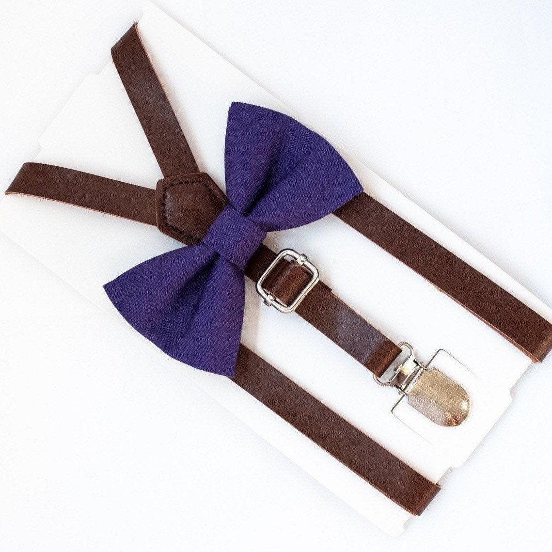 Close up of plum bow tie with brown suspenders and metal hardware on white background