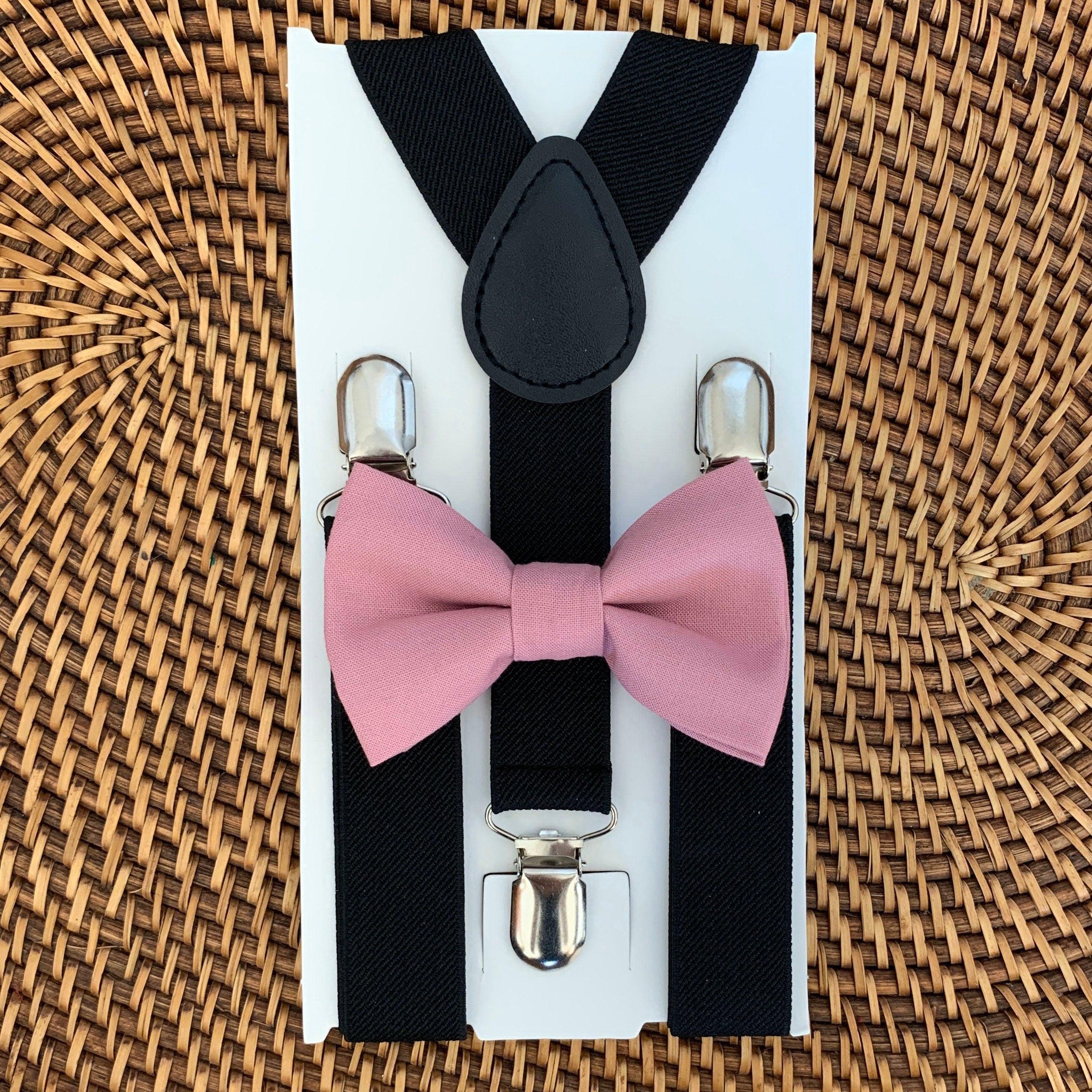 Black suspenders with pink bow ties in a box on a woven surface