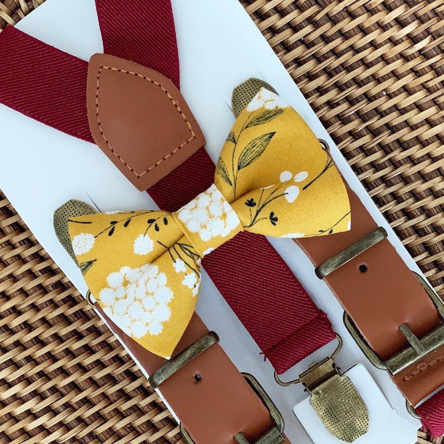 Mustard floral bow tie with burgundy buckle suspenders and brown leather accents on white packaging.