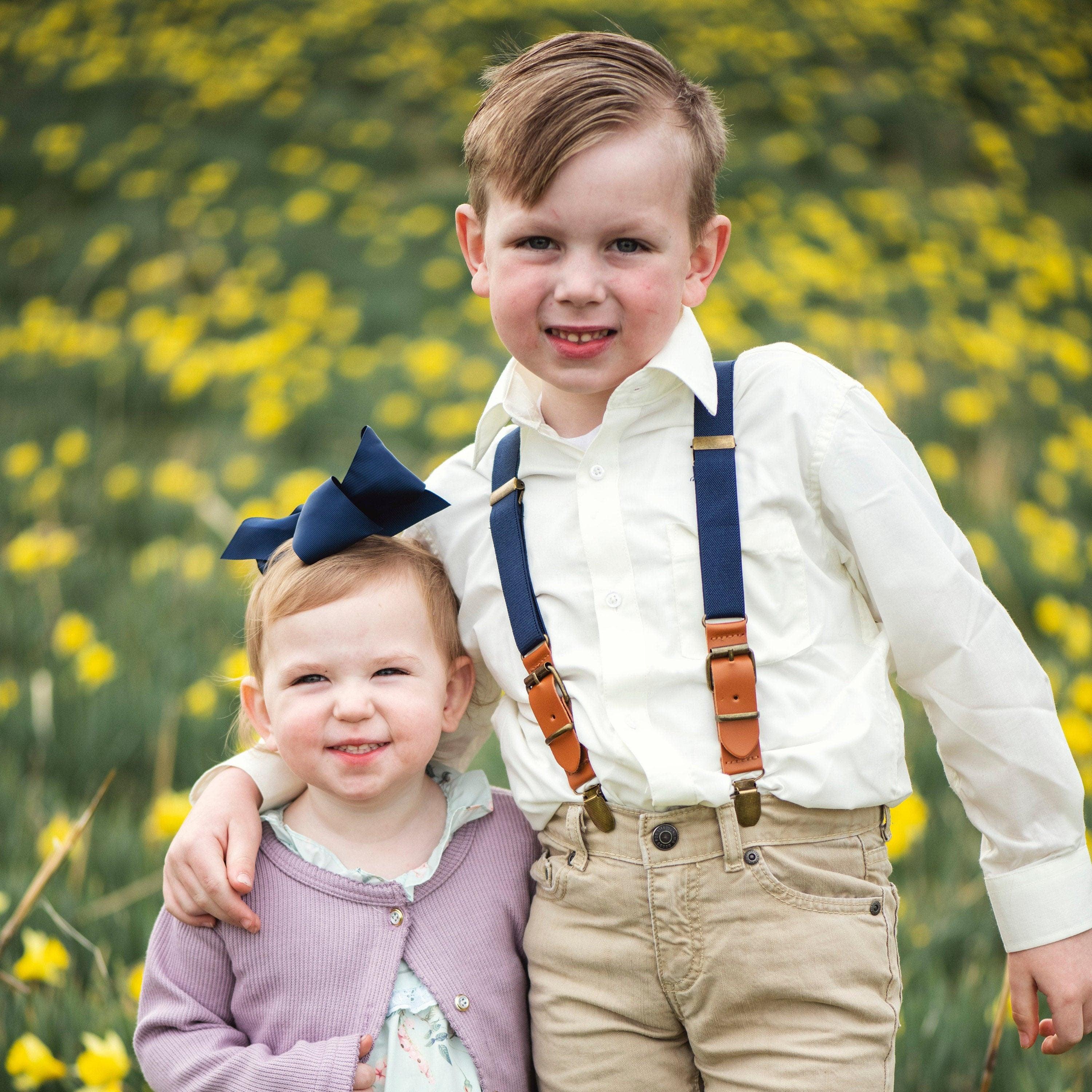 Navy blue ring bearer suspenders on a little boy hugging a little girl at a wedding.
