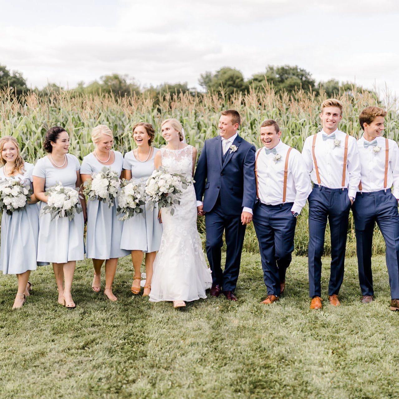 Wedding party outdoors in a cornfield with bridesmaids in pale blue dresses and groomsmen in white shirts with tan suspenders and slate bow ties