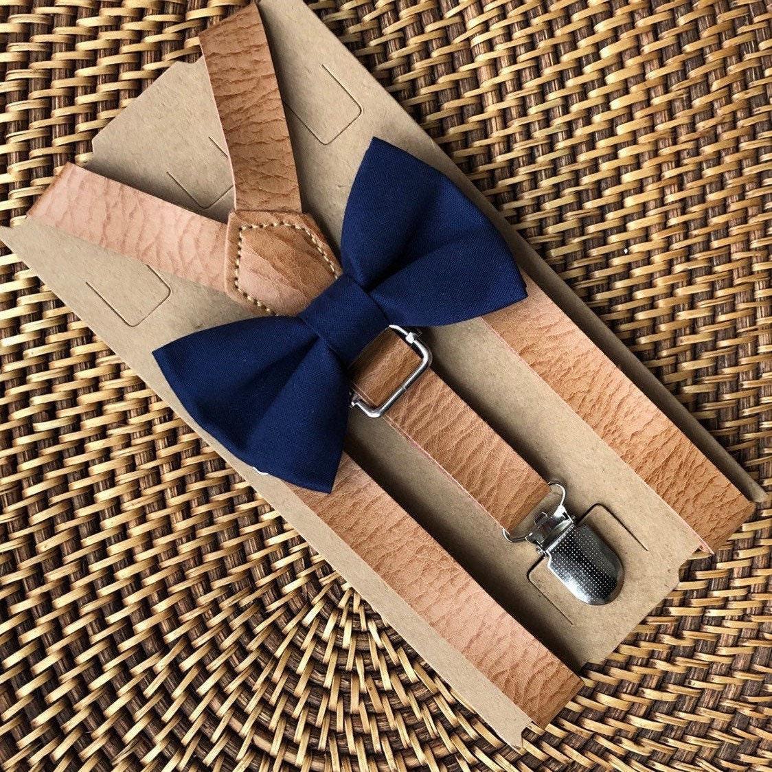 Navy bow tie with tan vegan leather suspenders displayed on brown cardboard packaging