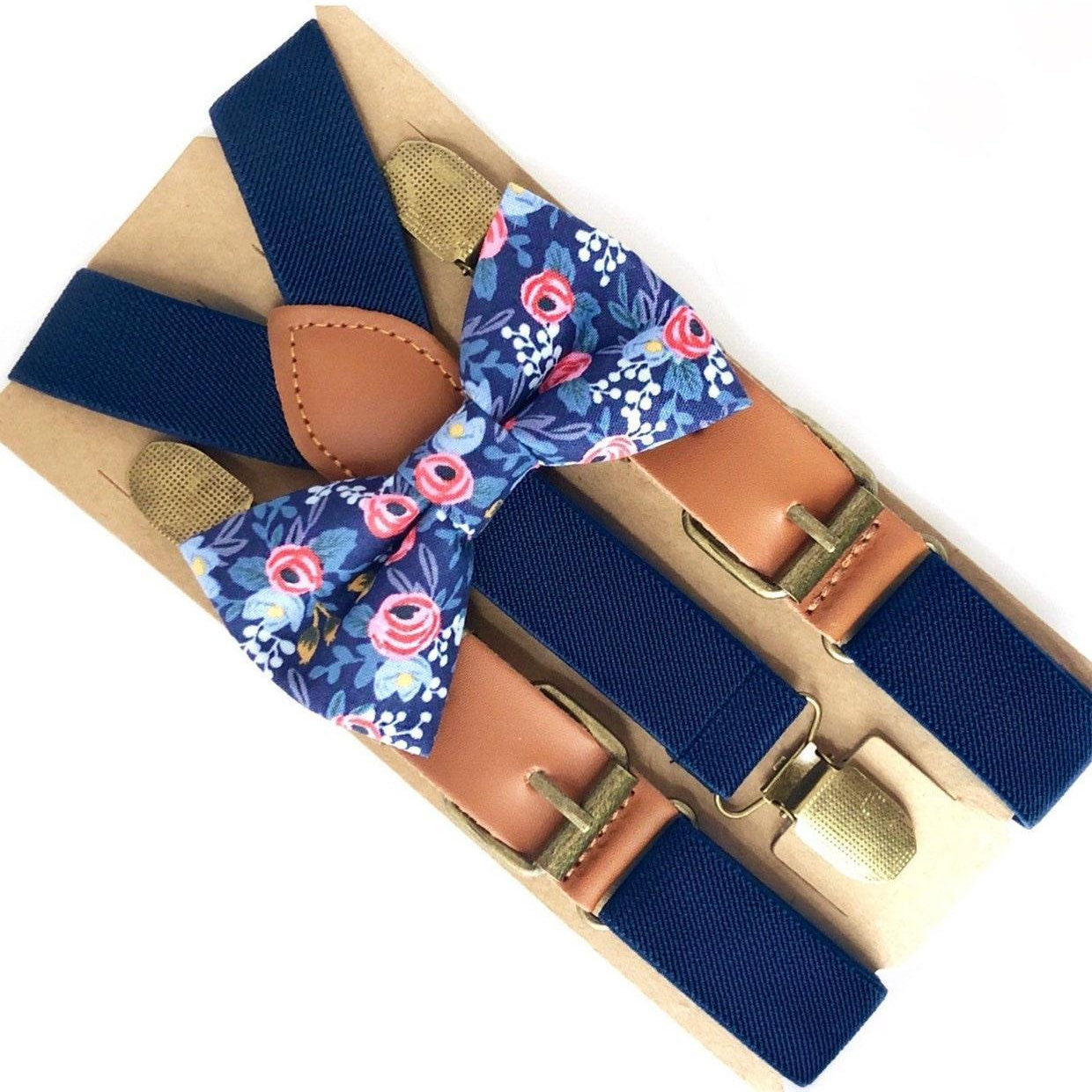Navy blue suspenders with a blue floral bow tie arranged on a tan cardboard backing with leather accents