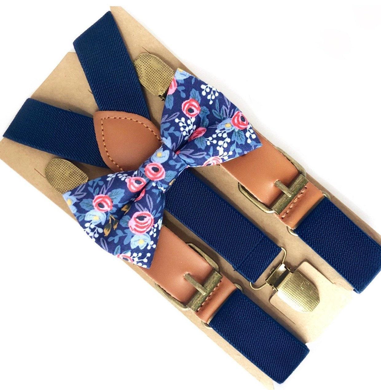 Navy blue suspenders with a blue floral bow tie arranged on a tan cardboard backing with leather accents