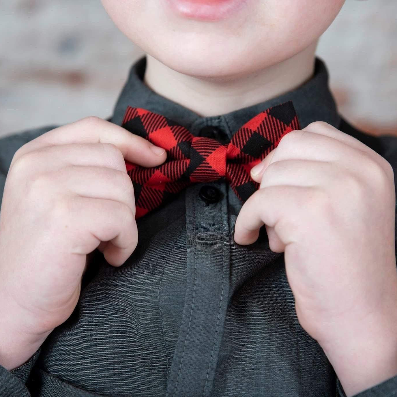 Close up of a child wearing a red buffalo plaid bow tie over a dark shirt