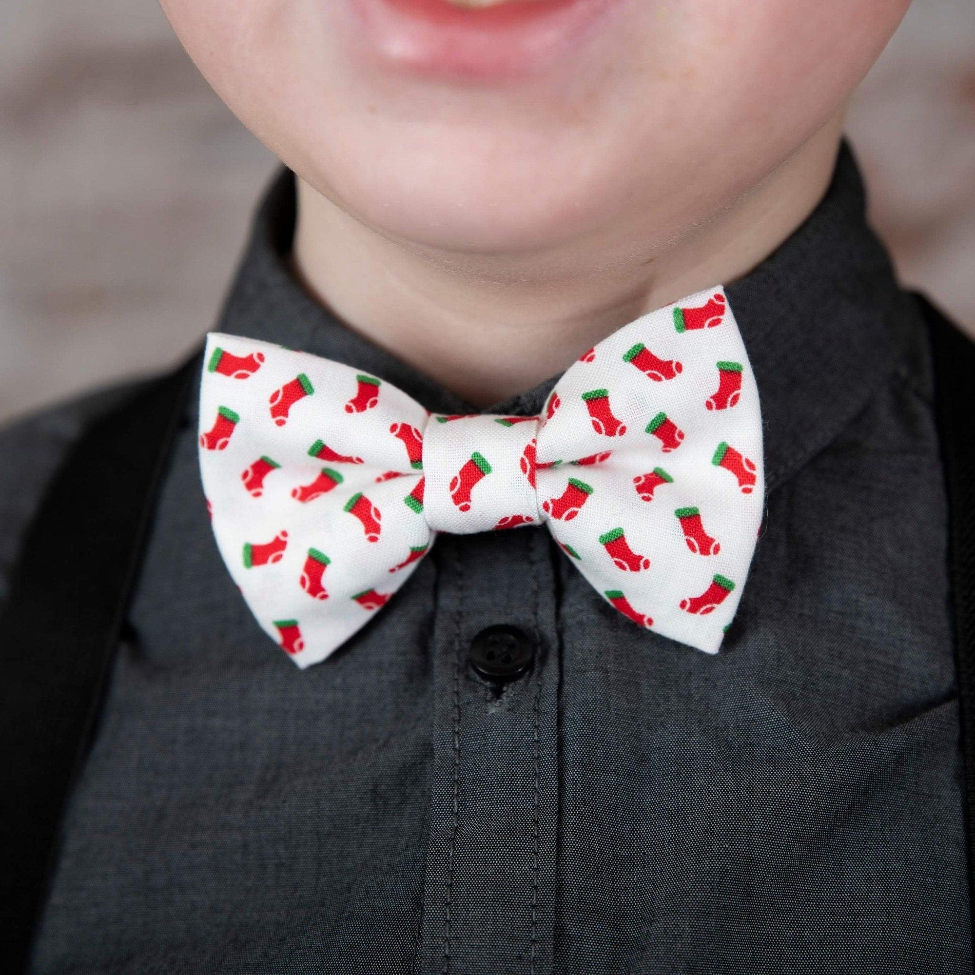 Festive white bow tie with red stocking pattern worn with dark brown vegan leather suspenders over a charcoal shirt