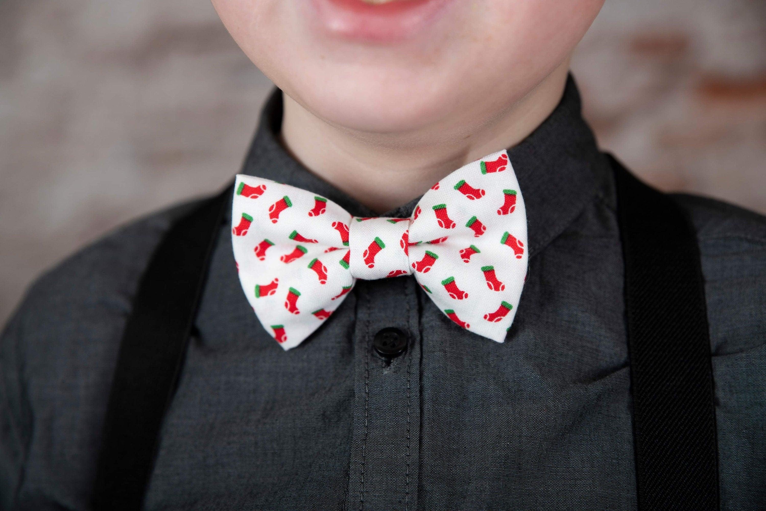 Festive white bow tie with red stocking pattern worn with dark brown vegan leather suspenders over a charcoal shirt