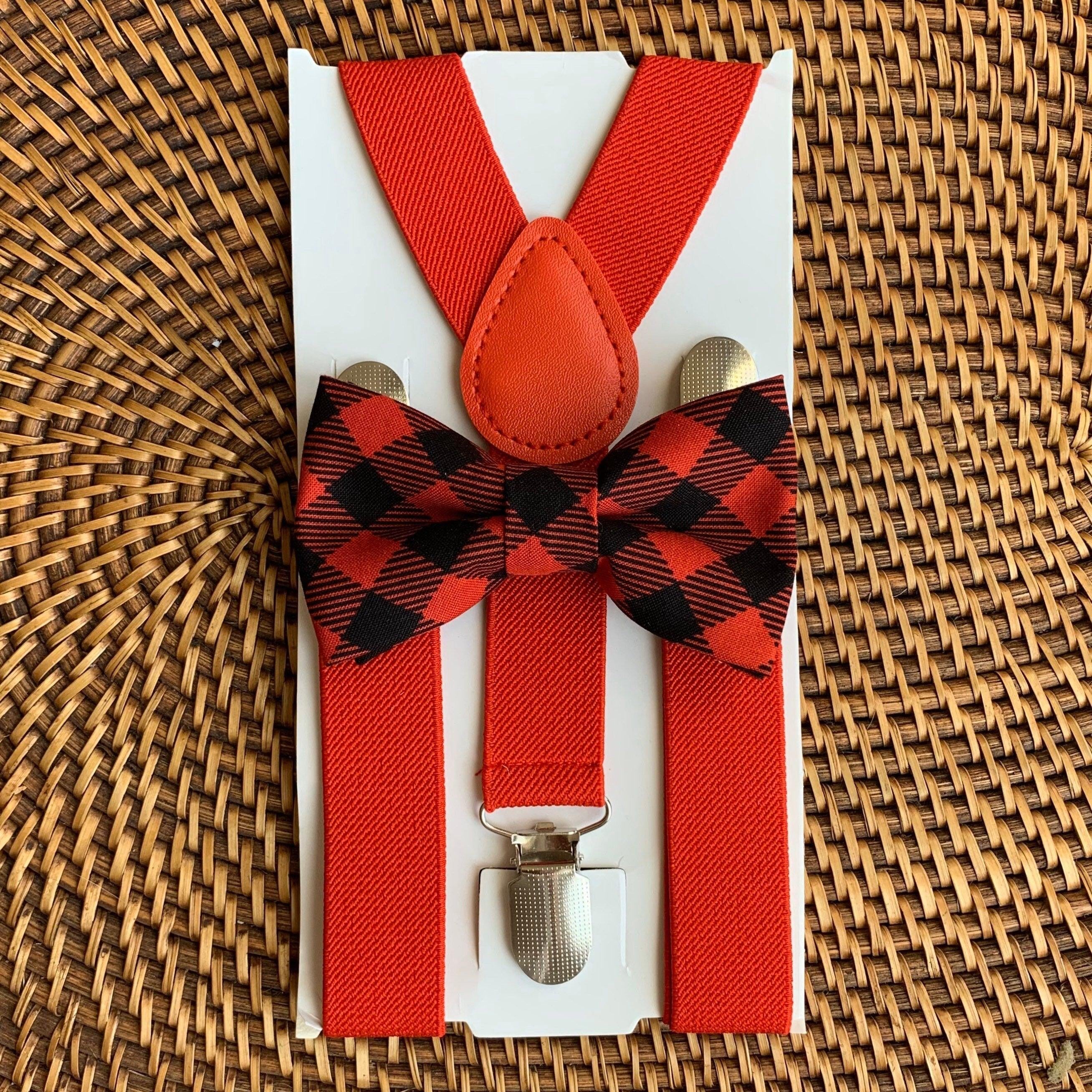 Close up of buffalo plaid red bow tie and red suspenders on white packaging against a woven wicker background.