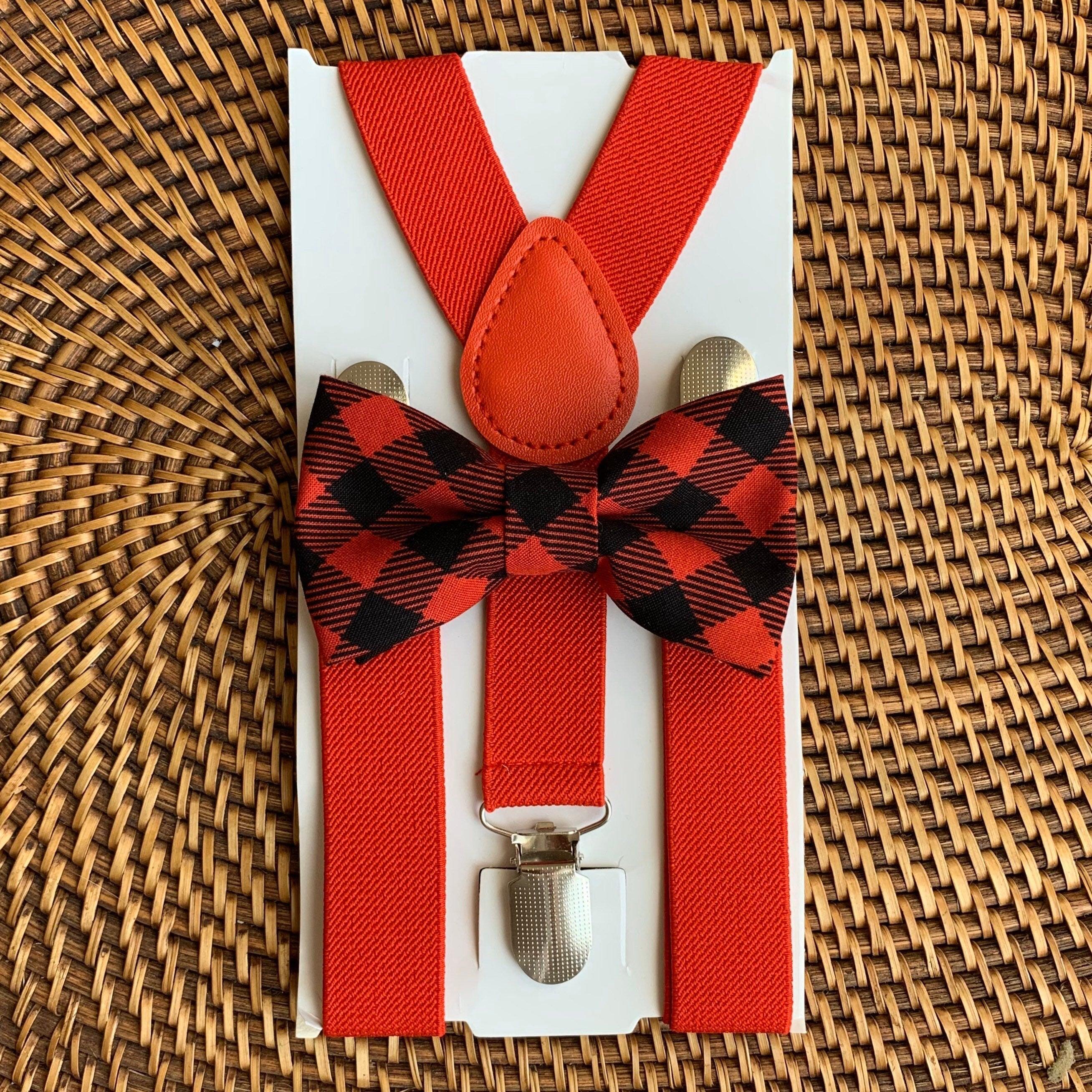 Close up of buffalo plaid red bow tie and red suspenders on white packaging against a woven wicker background.
