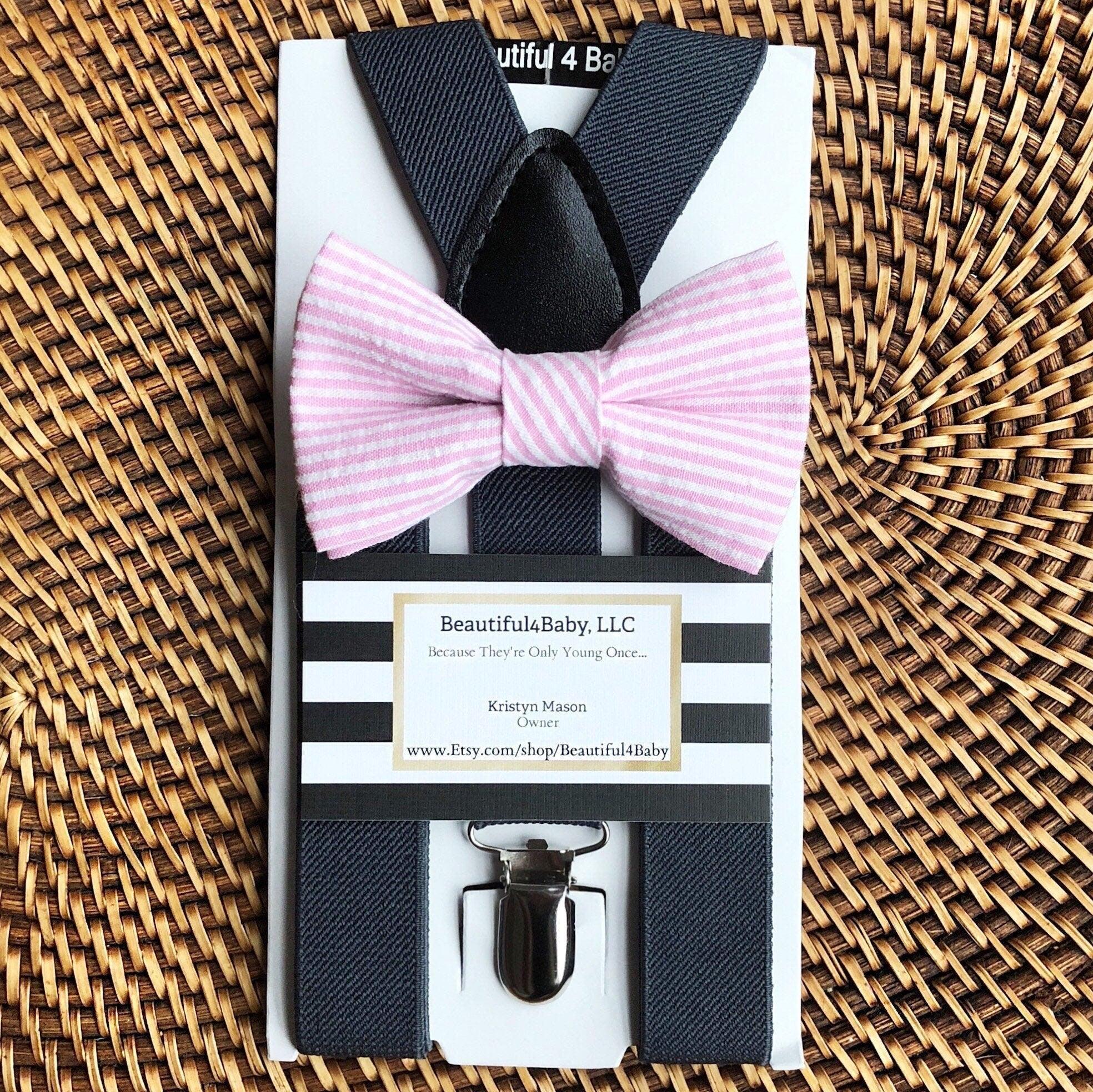 Gray suspenders and pink striped bow tie set in a striped box on a woven surface