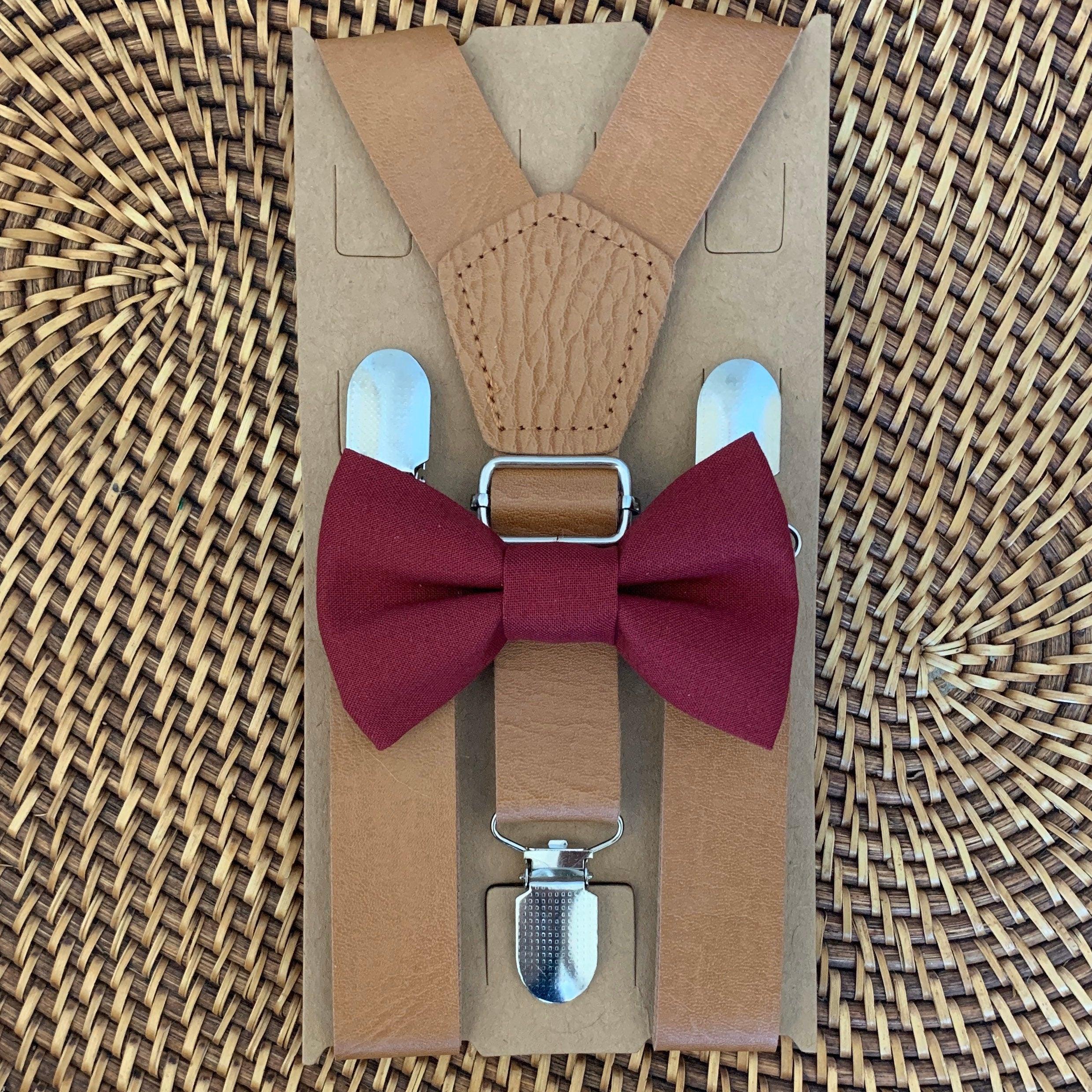 Close up of burgundy bow tie and tan suspenders arranged on kraft packaging against a woven background