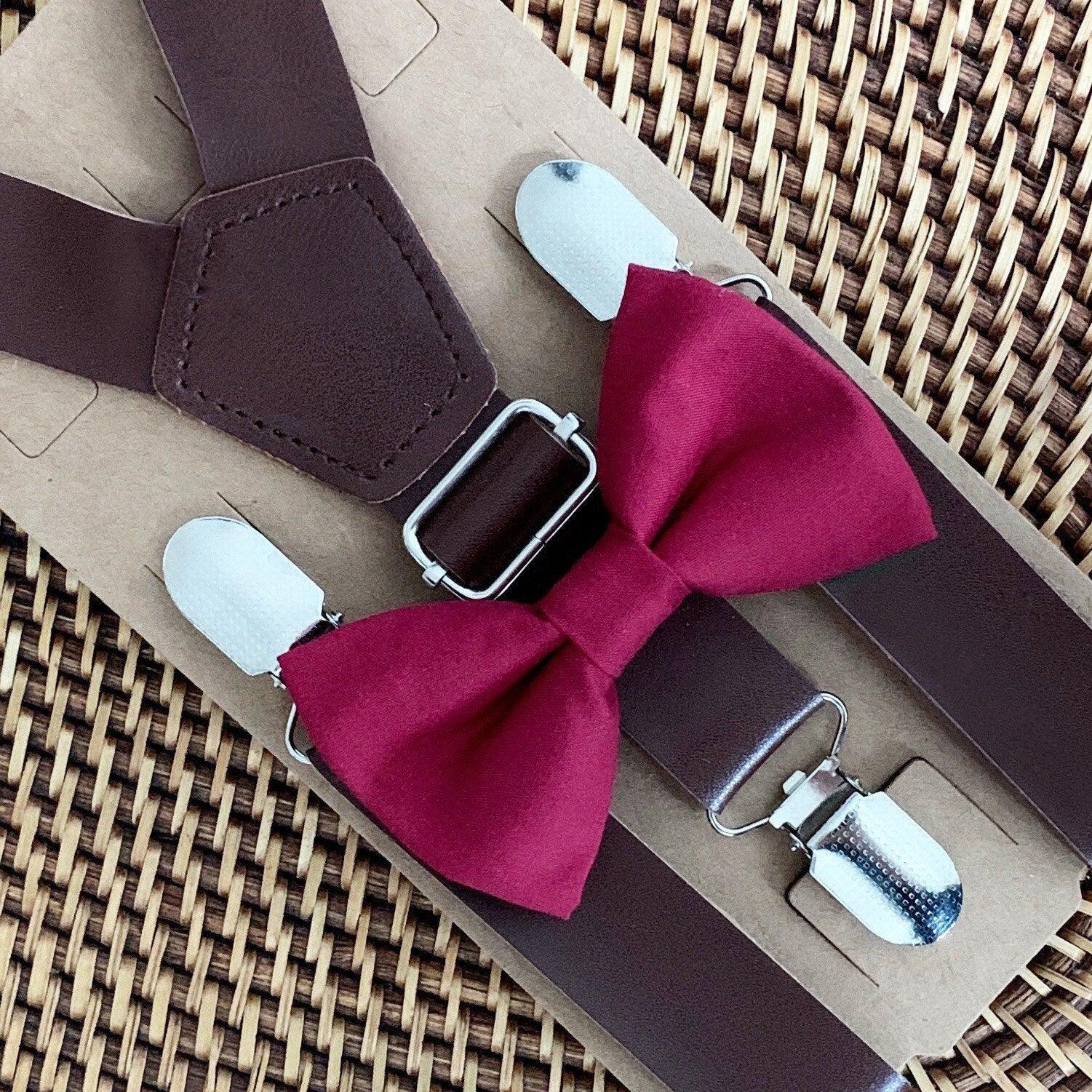 Brown suspenders with a burgundy bow tie on a woven surface
