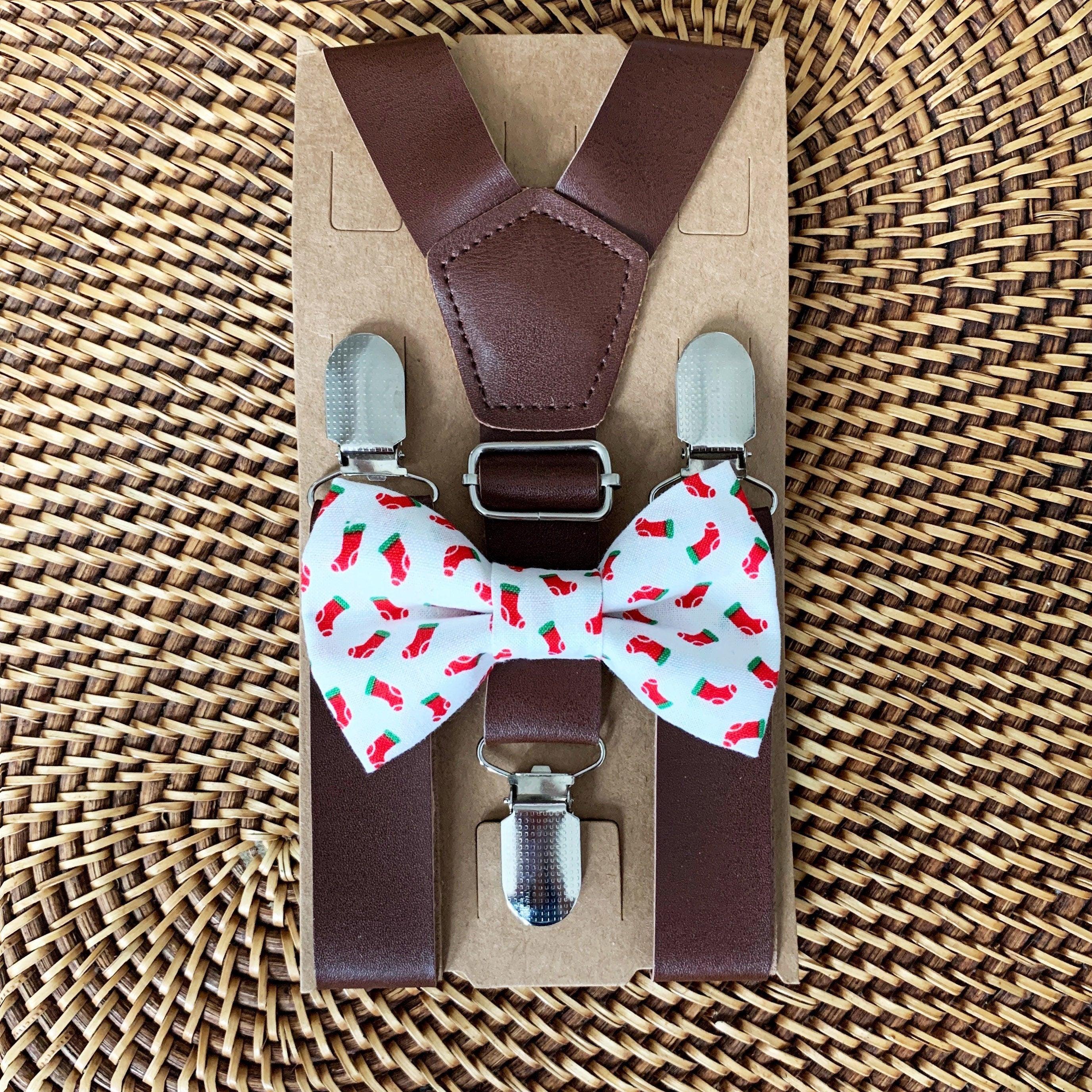 Top down view of a Christmas stocking bow tie with dark brown suspenders attached to a brown display card