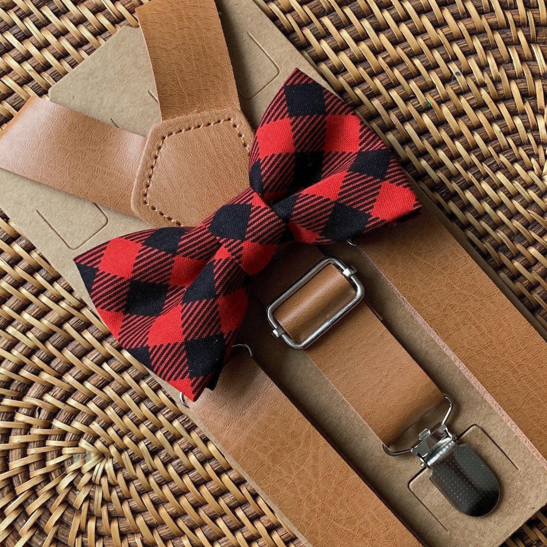 Red and black buffalo plaid bow tie with brown vegan leather suspenders on a brown leather surface.