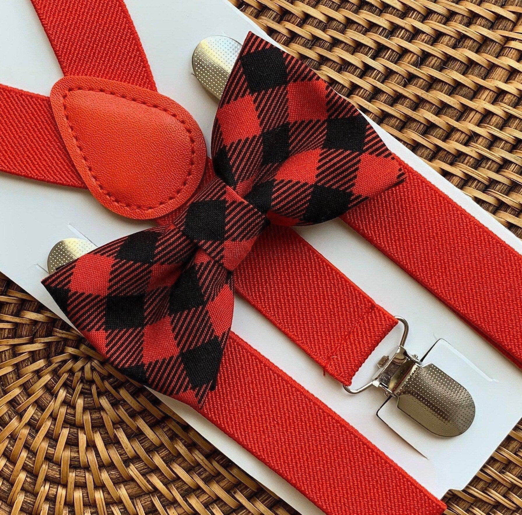 Close-up of red buffalo plaid bow tie with matching red suspenders laid on a white card over a woven surface.
