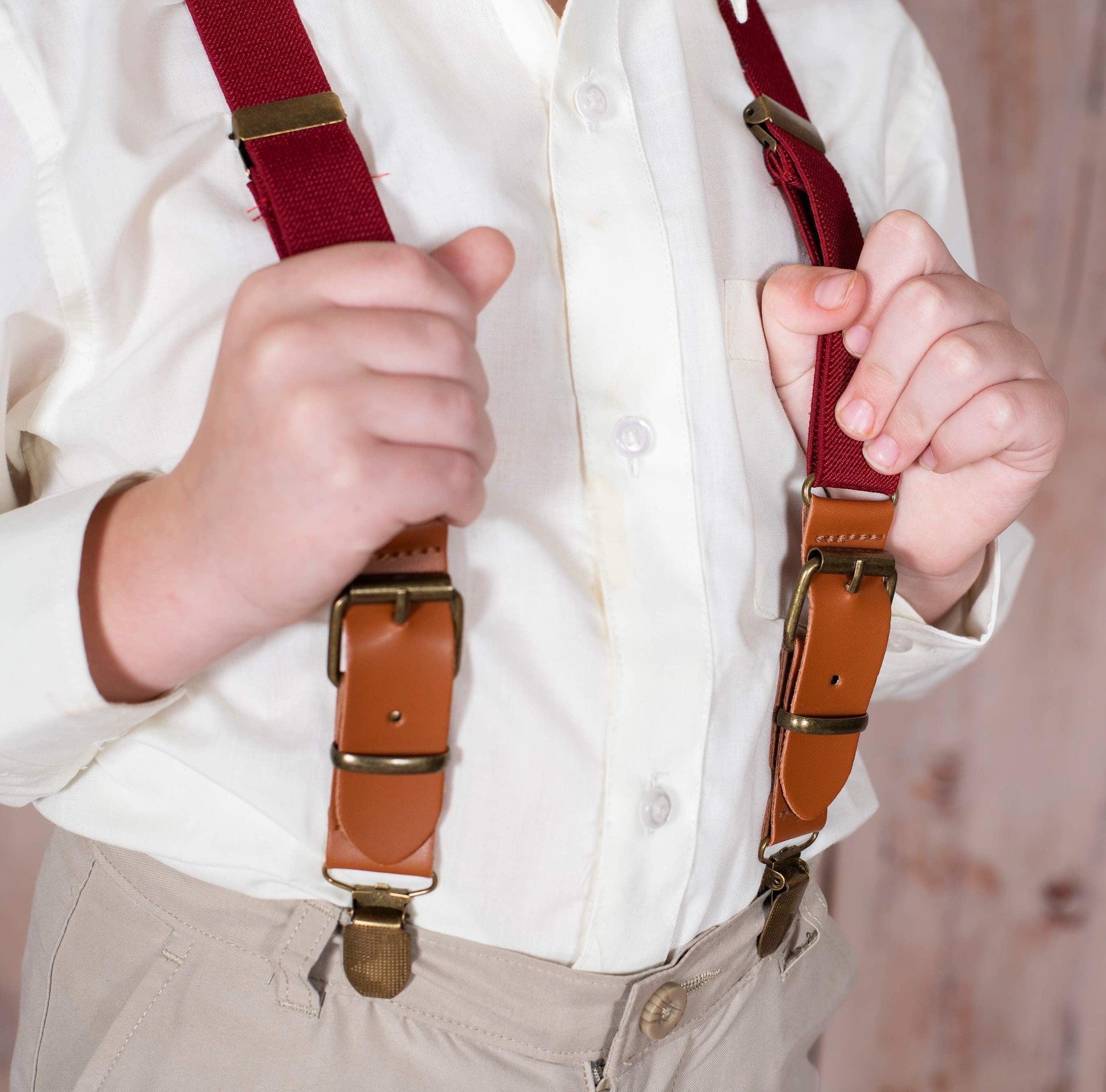 Close-up of a child wearing a white shirt with burgundy suspenders and brass clips.