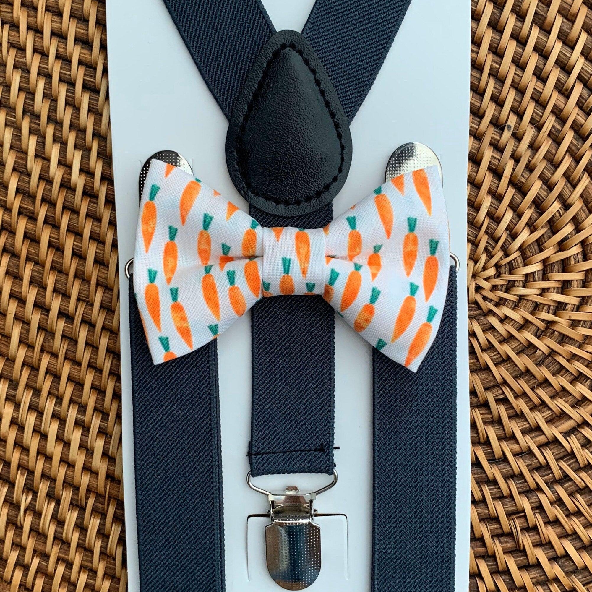 Front view of a carrot print bow tie paired with dark gray suspenders on a pale blue display card