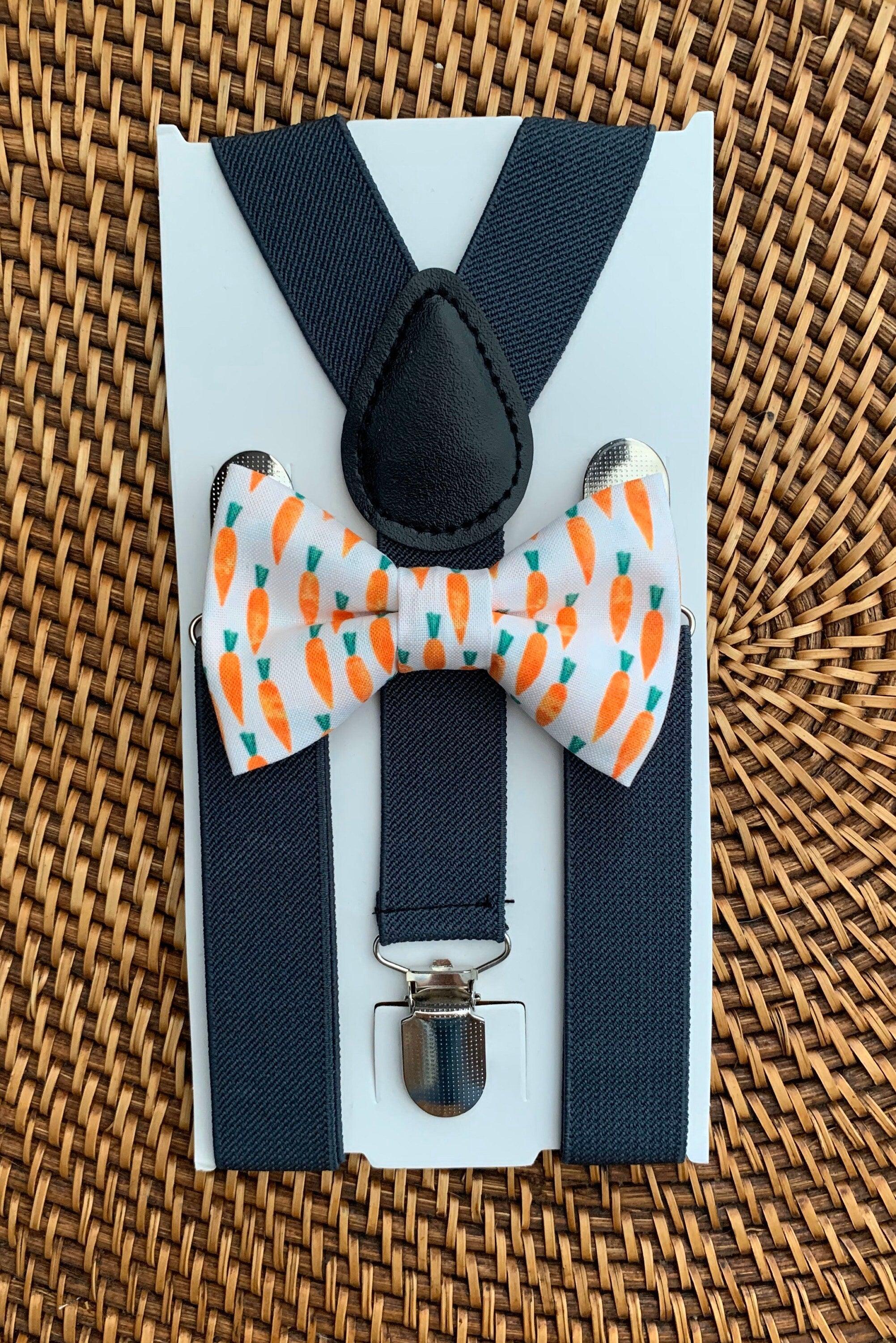 Front view of a carrot print bow tie paired with dark gray suspenders on a pale blue display card
