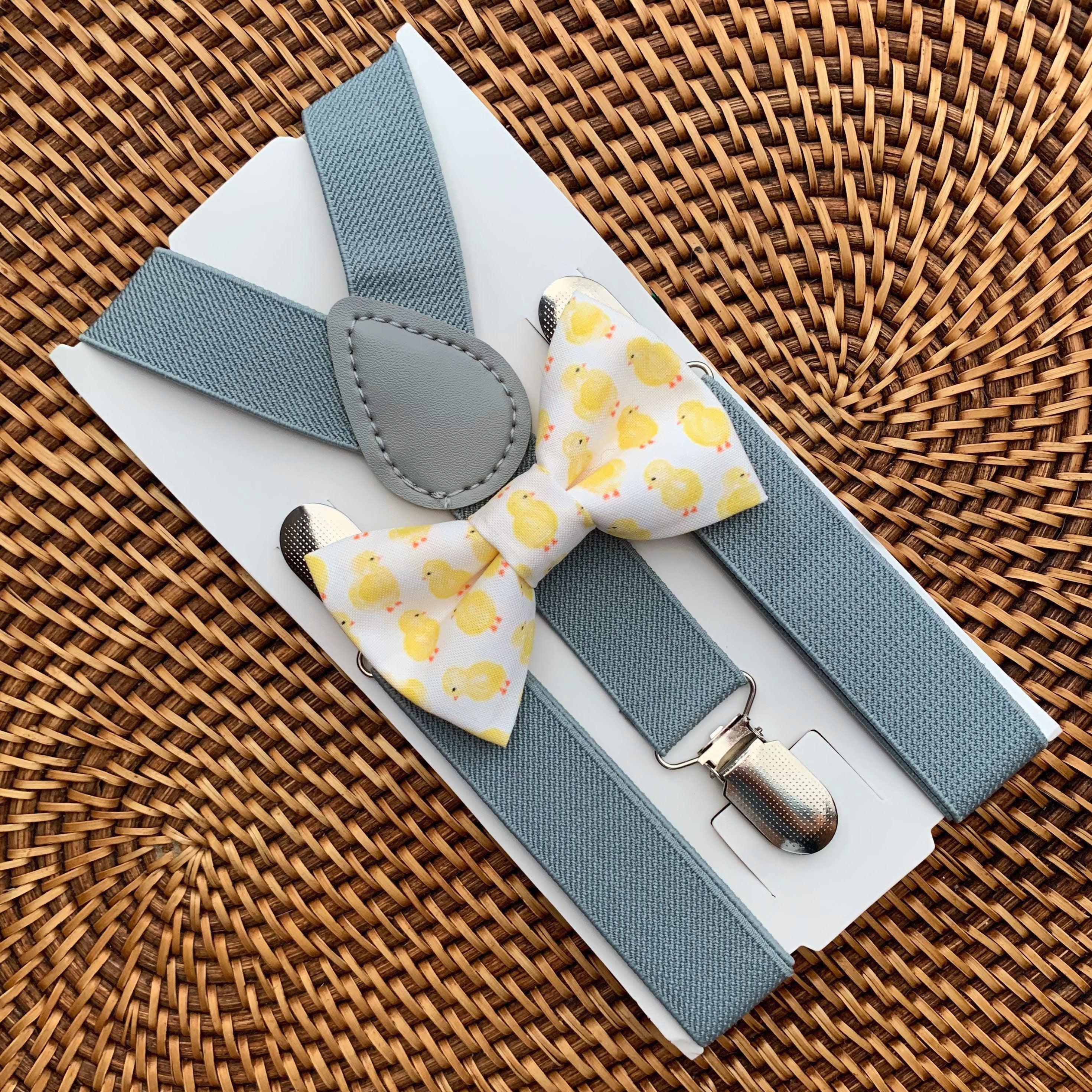 Light grey suspenders and a chick print bow tie on a white card against a woven rattan background.