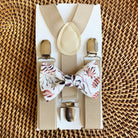 A set of tan suspenders and an autumn floral bow tie laid out on a woven surface.