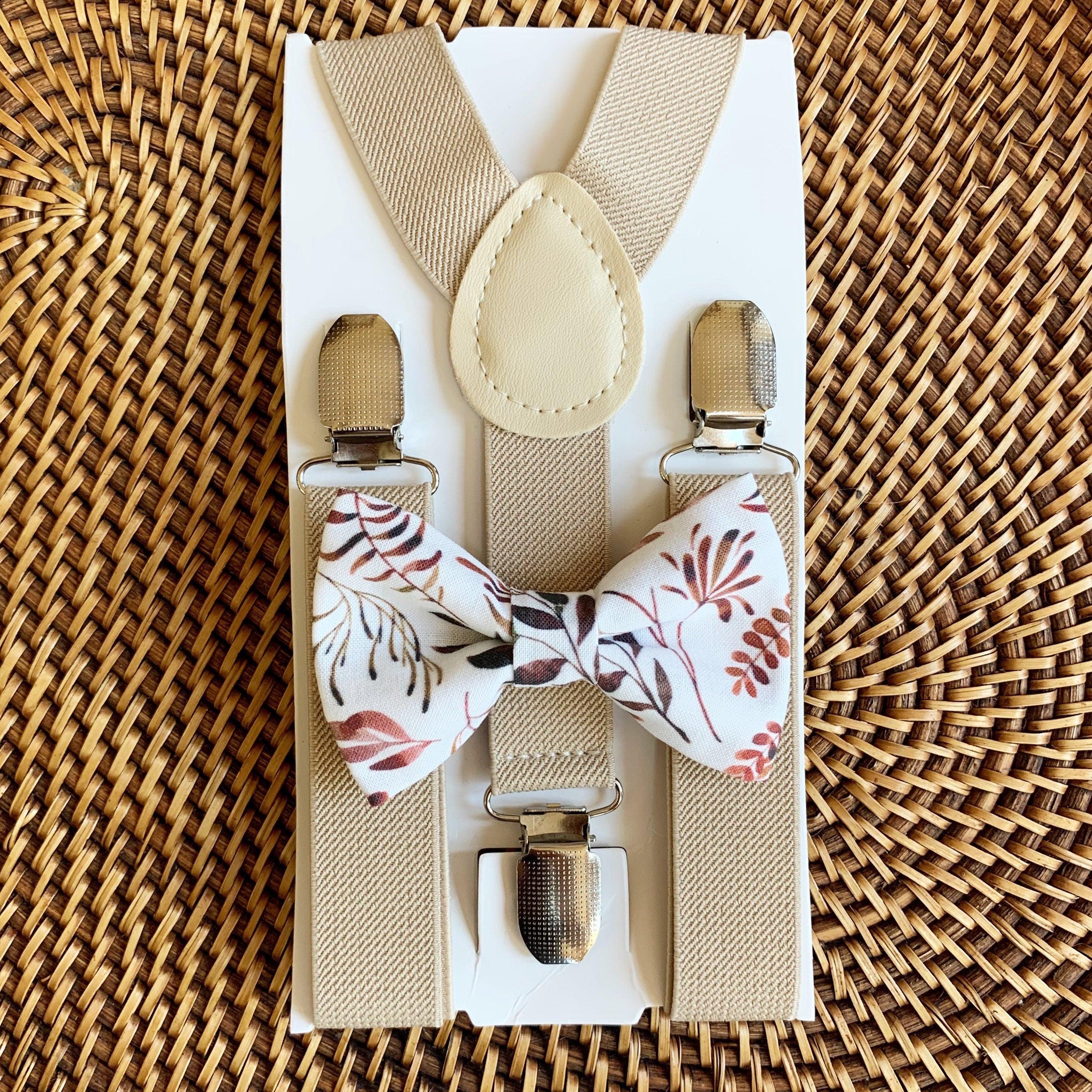 A set of tan suspenders and an autumn floral bow tie laid out on a woven surface.