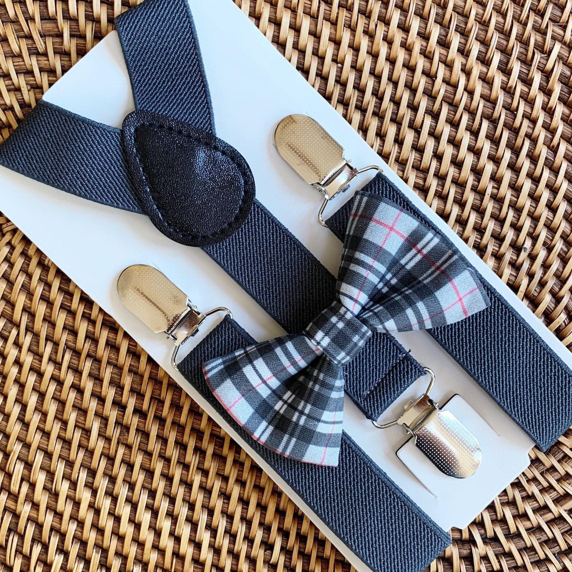 Gray plaid bow tie and matching suspenders with metal clips laid out on a white surface