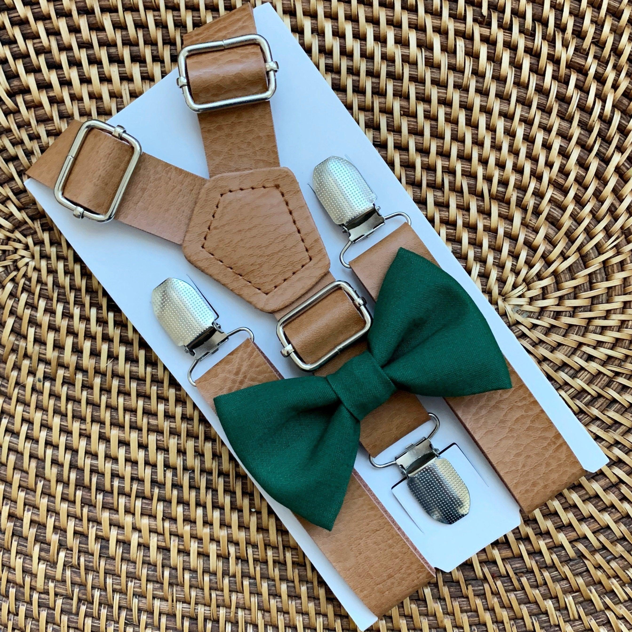 Emerald green bow tie with tan vegan leather suspenders displayed on a white card against a woven background.