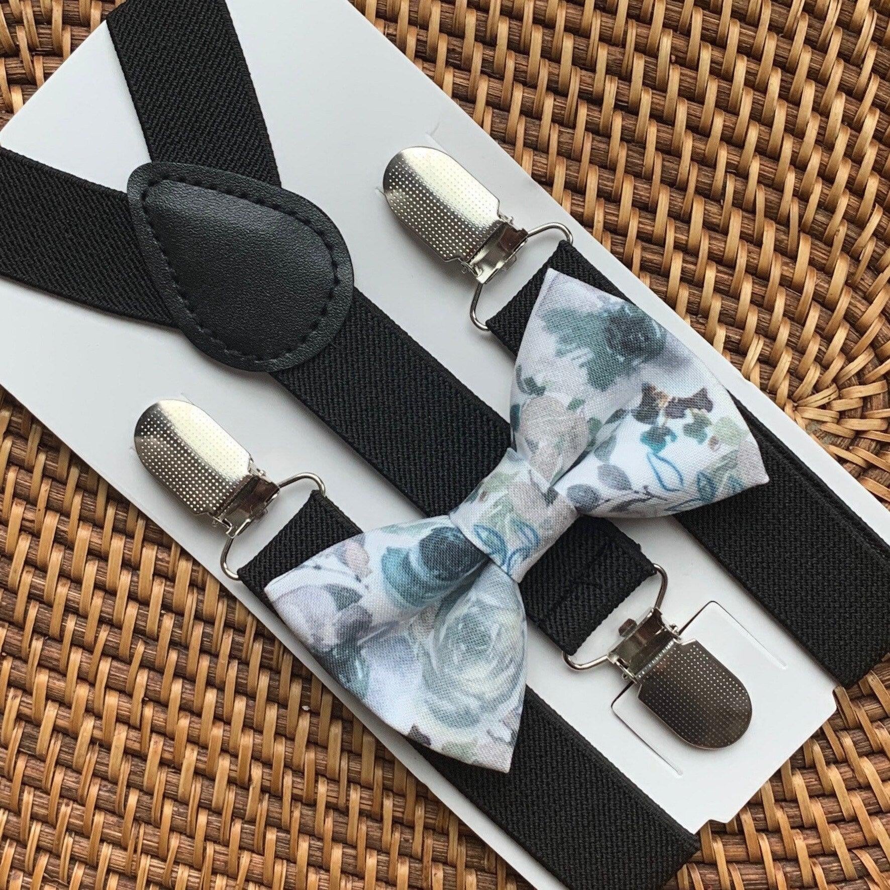 Grey and blue floral bow tie paired with black suspenders displayed on a white card against a wicker background.