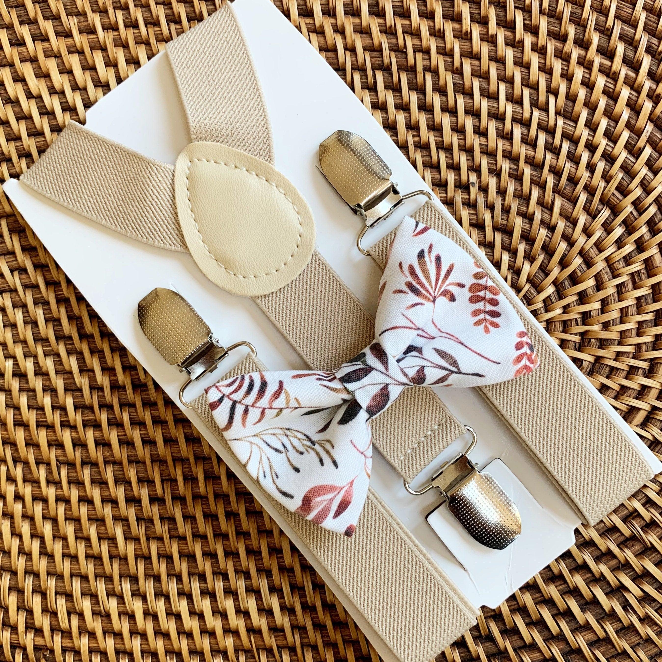 A set of tan suspenders and an autumn floral bow tie laid out on a woven surface.