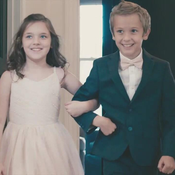 Ring bearer in blush bow tie walking with flower girl in a blush dress.