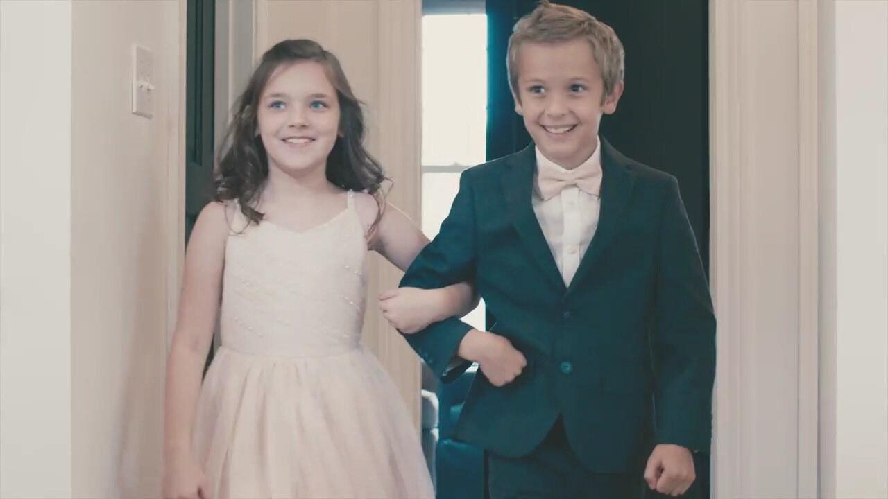 Ring bearer in blush bow tie walking with flower girl in a blush dress.