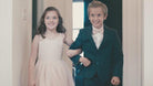 Ring bearer in blush bow tie walking with flower girl in a blush dress.