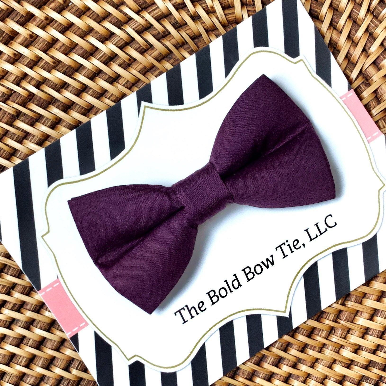 Product graphic showcasing the back of a pre-tied bow tie in a red and black buffalo plaid pattern, resting on a rustic wood surface. Two black elastic loops are attached to the center knot to slide onto a pet collar. Overlay text reads: Back of Bow Tie (may not be actual bow tie in listing).