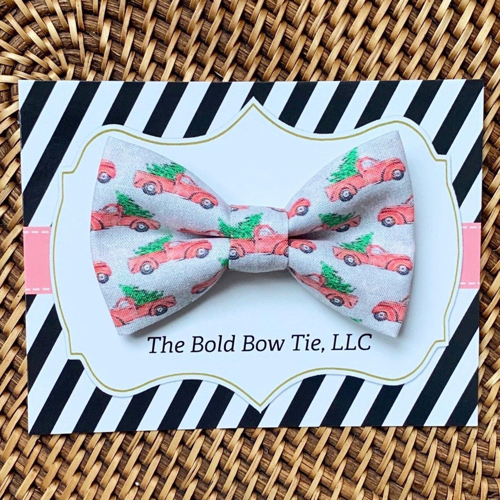 Gray Christmas truck bow tie for dogs featuring red trucks and green trees on decorative packaging