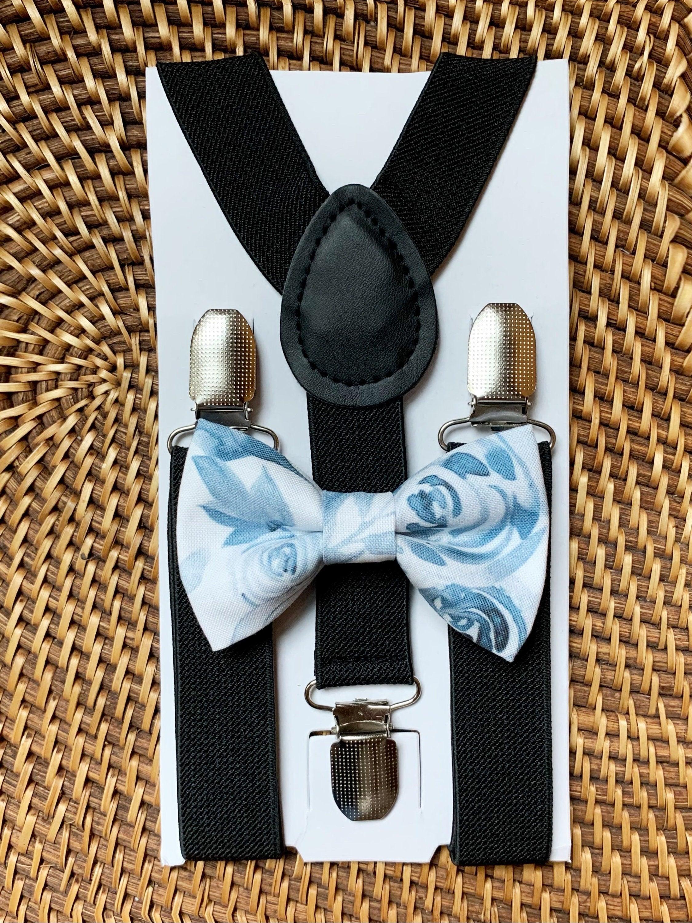 A children's suspenders and bow tie set displayed on a white backing card. The suspenders are black with silver metal clips, and the matching bow tie has a light blue and white floral rose pattern.